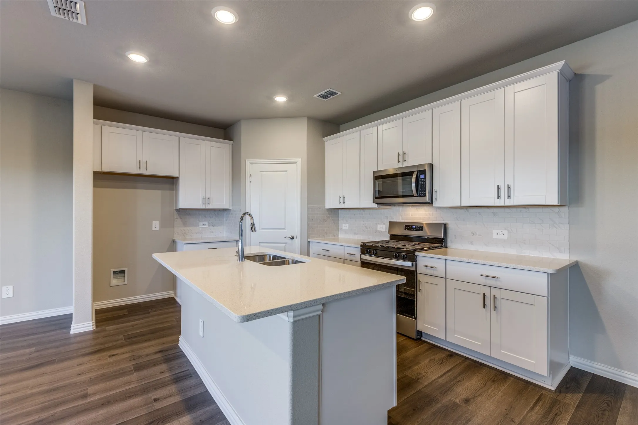 Kitchen featuring a center island with sink, dark hardwood / wood-style floors, stainless steel appliances, and white cabinets