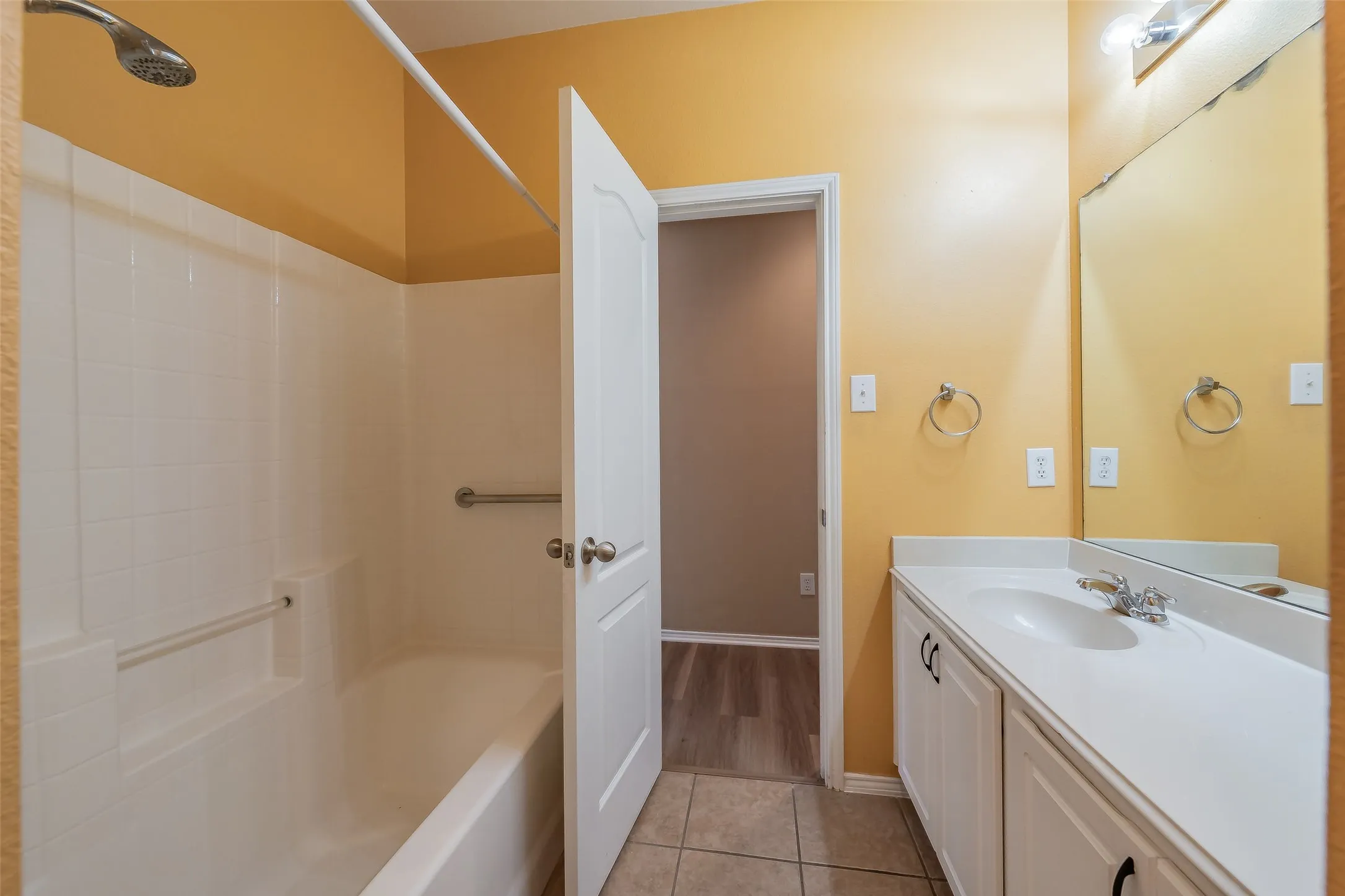 Bathroom featuring a built-in bathtub with shower, white tile surround, and grab bars