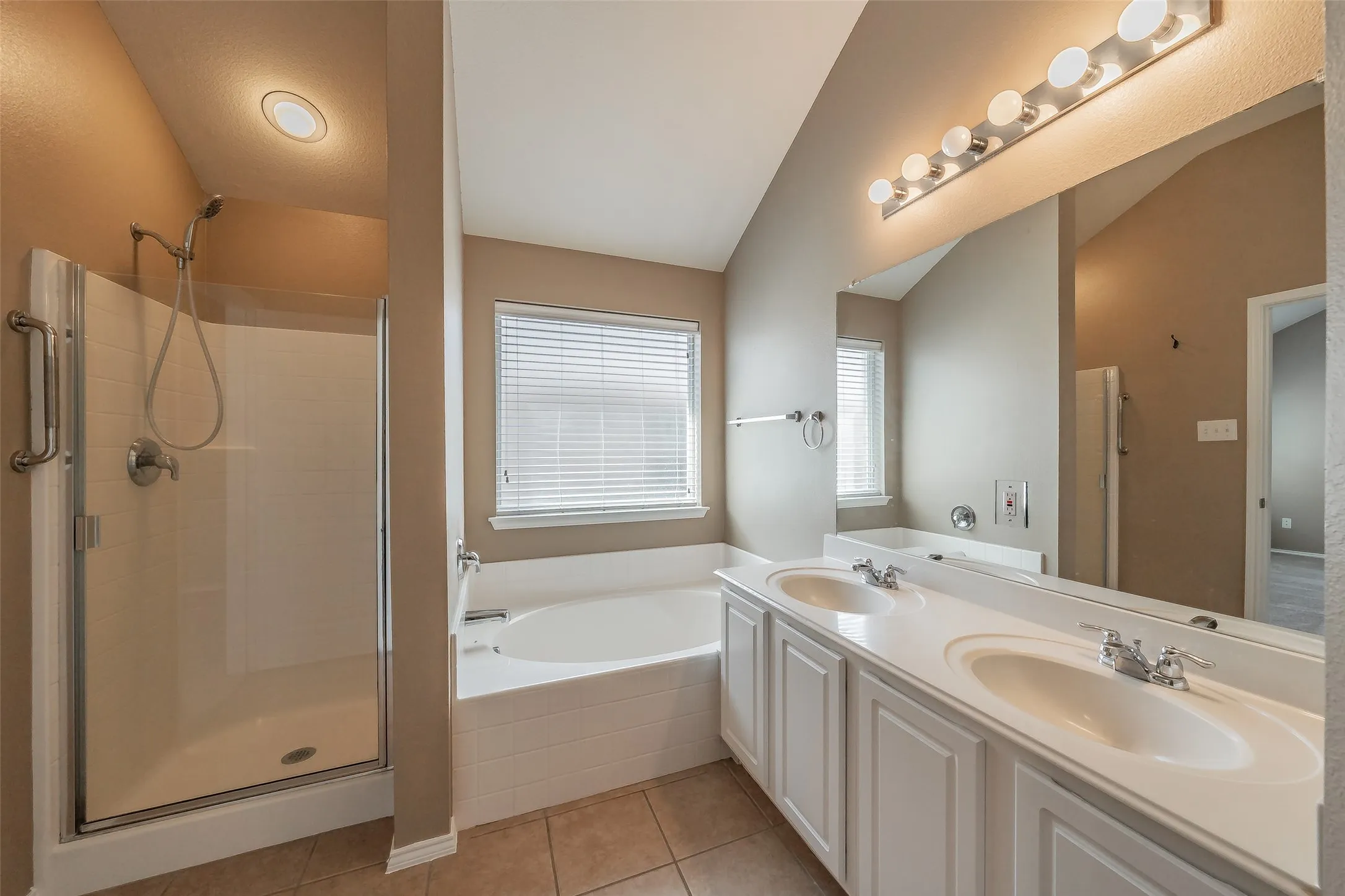 Bathroom featuring a dual-sink vanity, tiled flooring, built-in bathtub, and a glass-enclosed shower