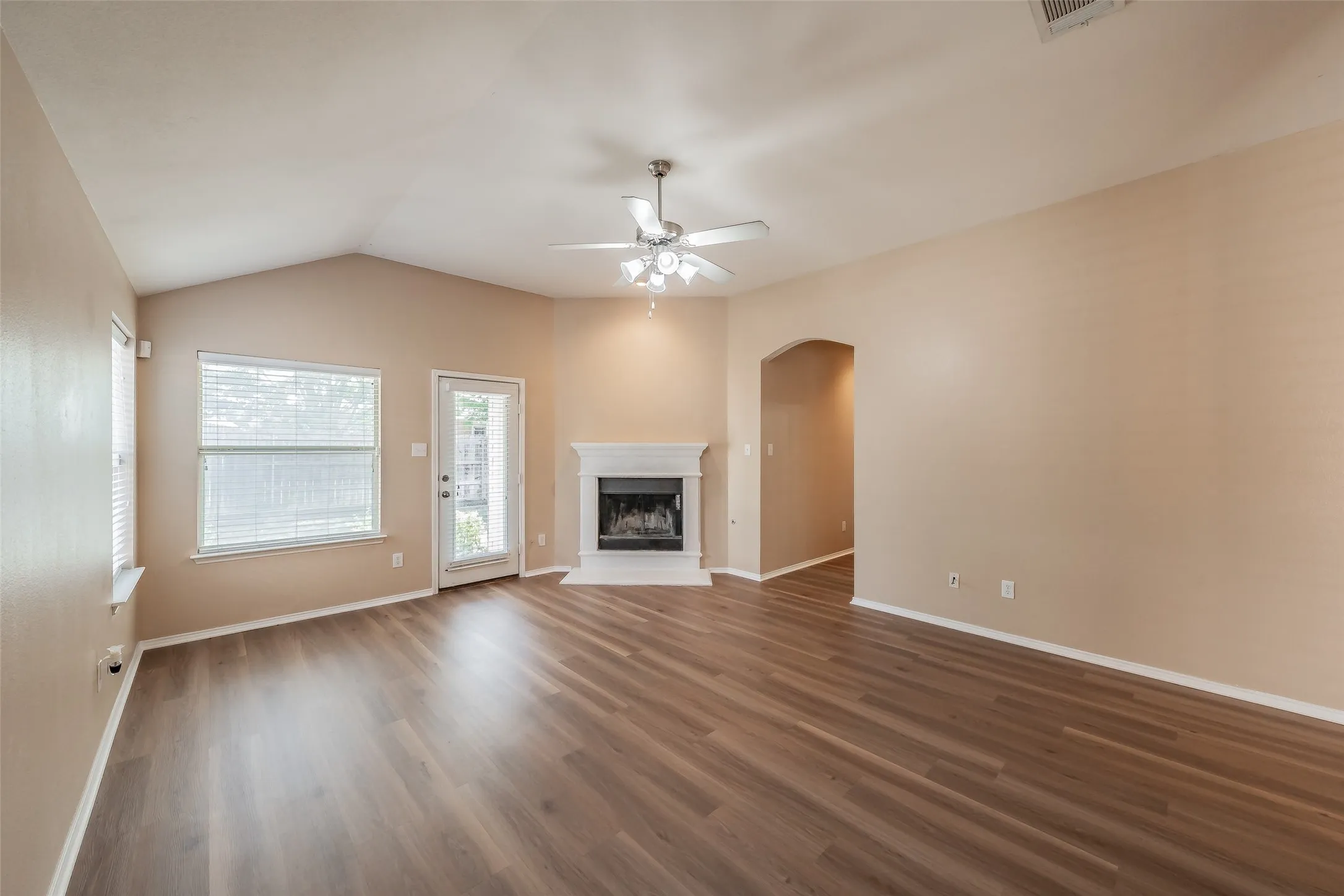 Vaulted ceiling with ceiling fan, wood-finish flooring, fireplace with mantel, and an arched entryway