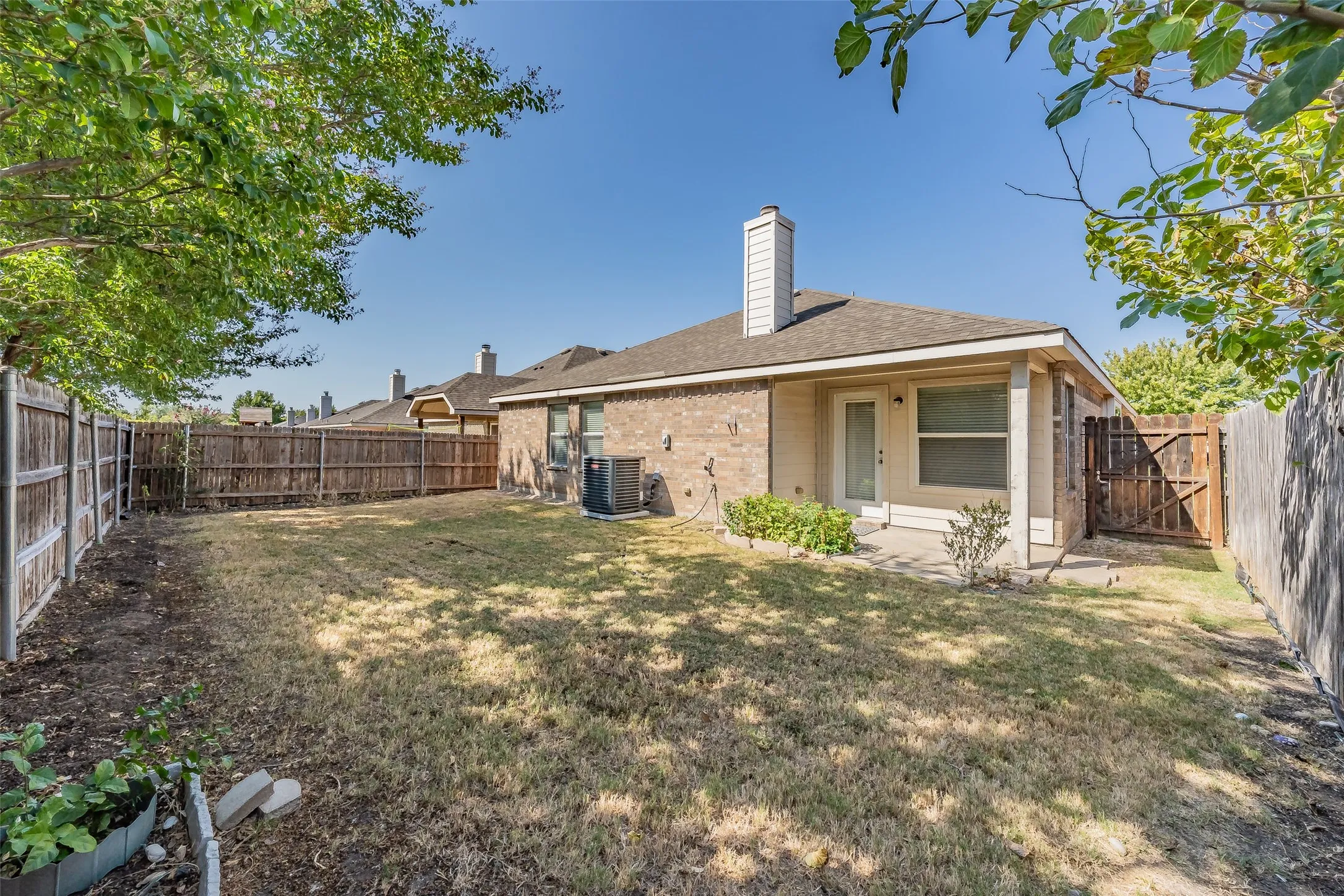 Fenced backyard featuring a covered patio with a glass-paneled door and a wood gate