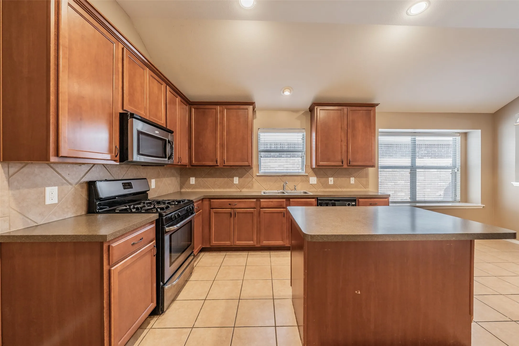 Kitchen featuring wood-finish cabinetry, stainless steel appliances, a center island with a countertop, tile flooring, and recessed lighting