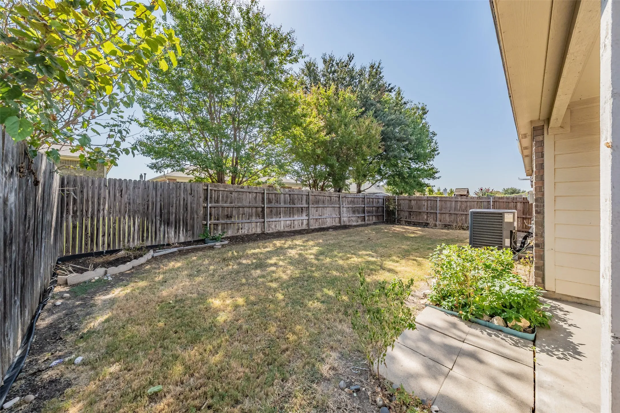 Enclosed backyard with a wood privacy fence, concrete patio area, and established plantings