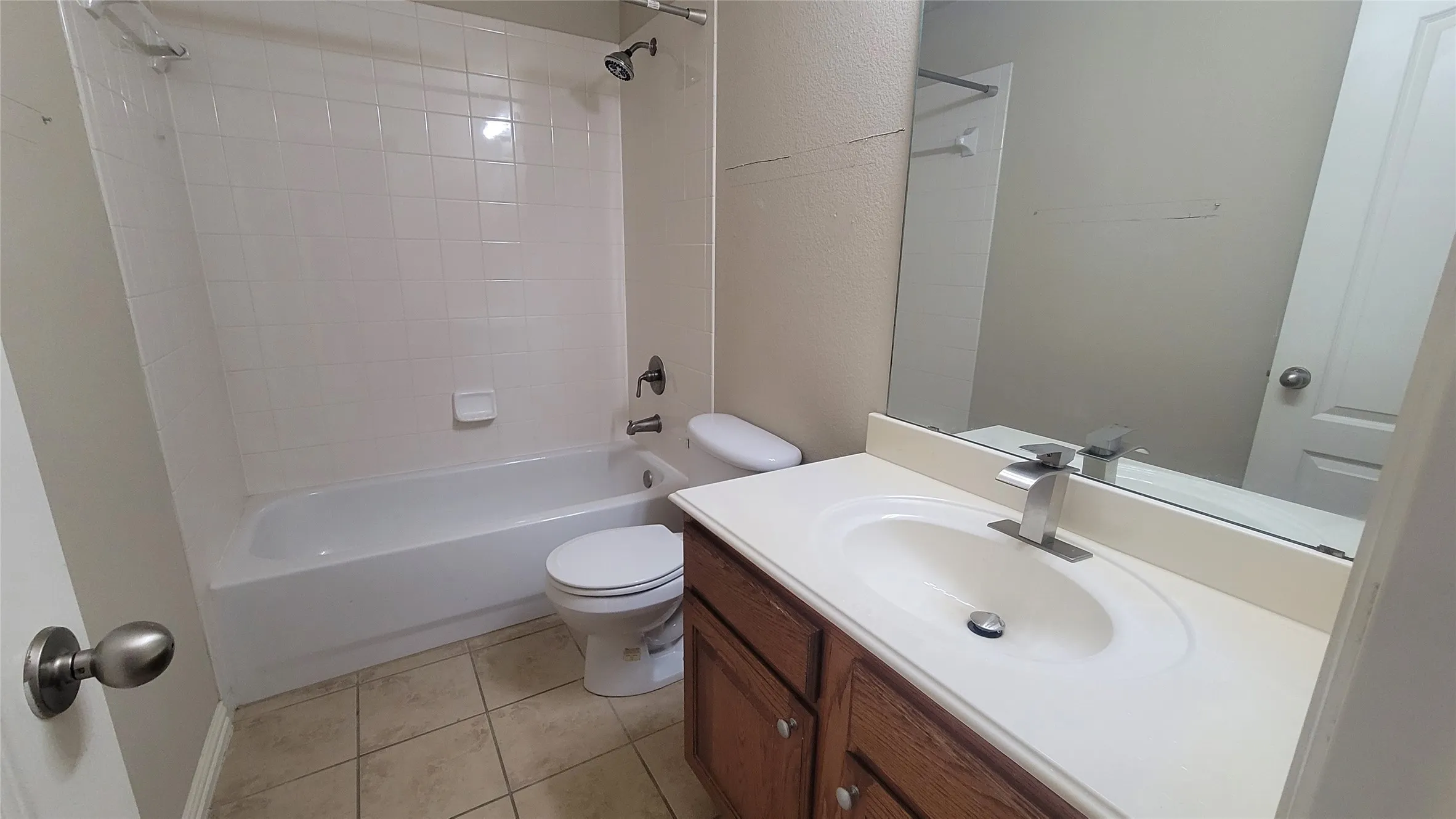 Bathroom featuring a white bathtub, white tiled shower surround, toilet, wood-finish vanity with an integrated sink, and a wall-mounted mirror