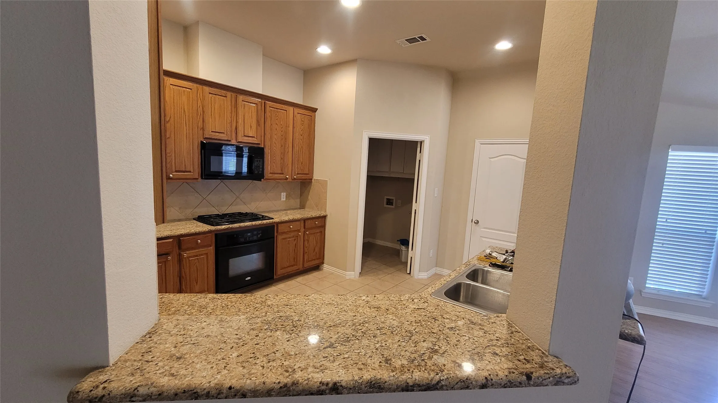 Kitchen featuring granite countertops, wood cabinetry, built-in oven, and a double basin stainless steel sink