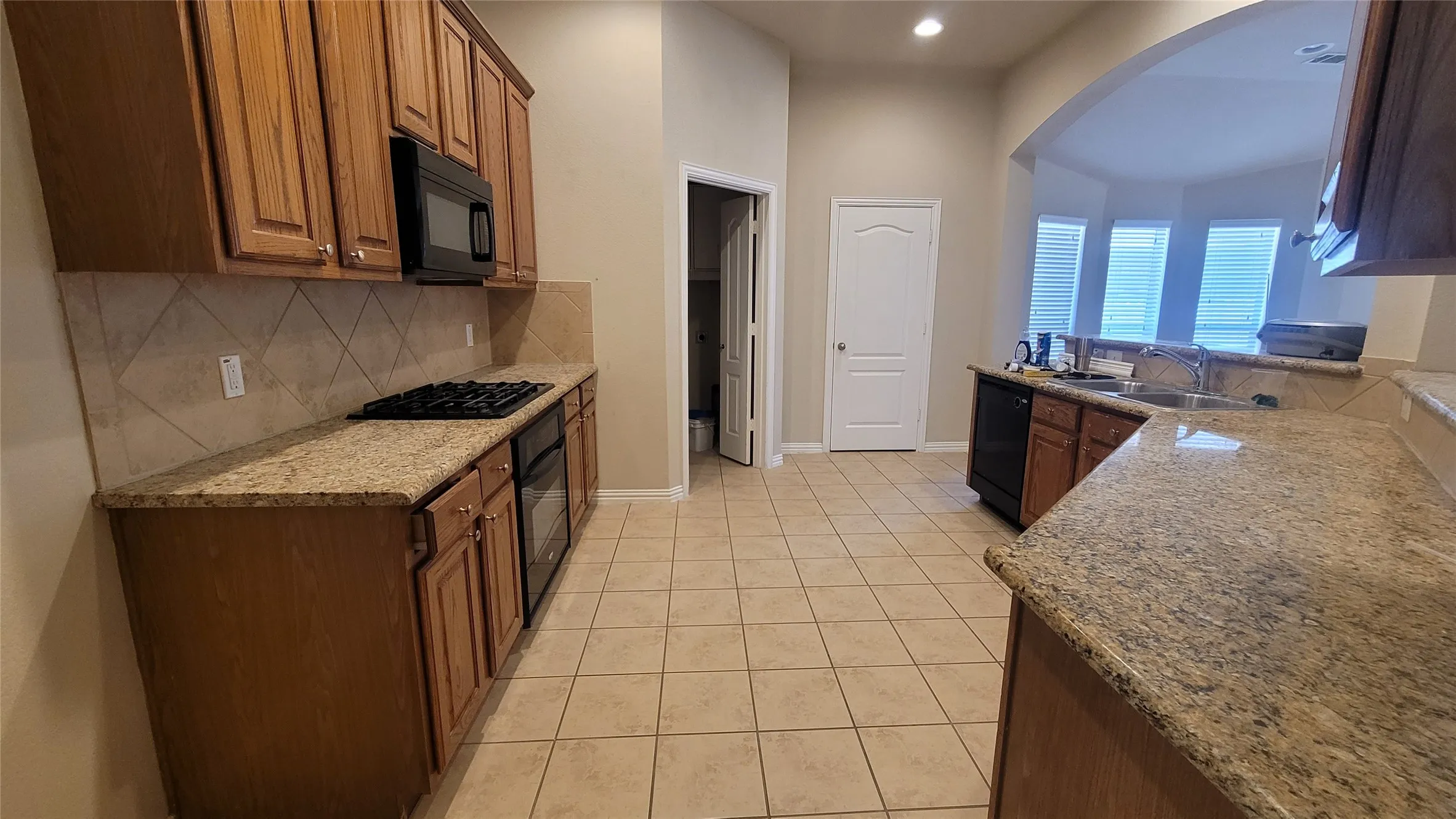 Kitchen featuring tile flooring, wood cabinetry, stone countertops, a built-in microwave, and a gas cooktop