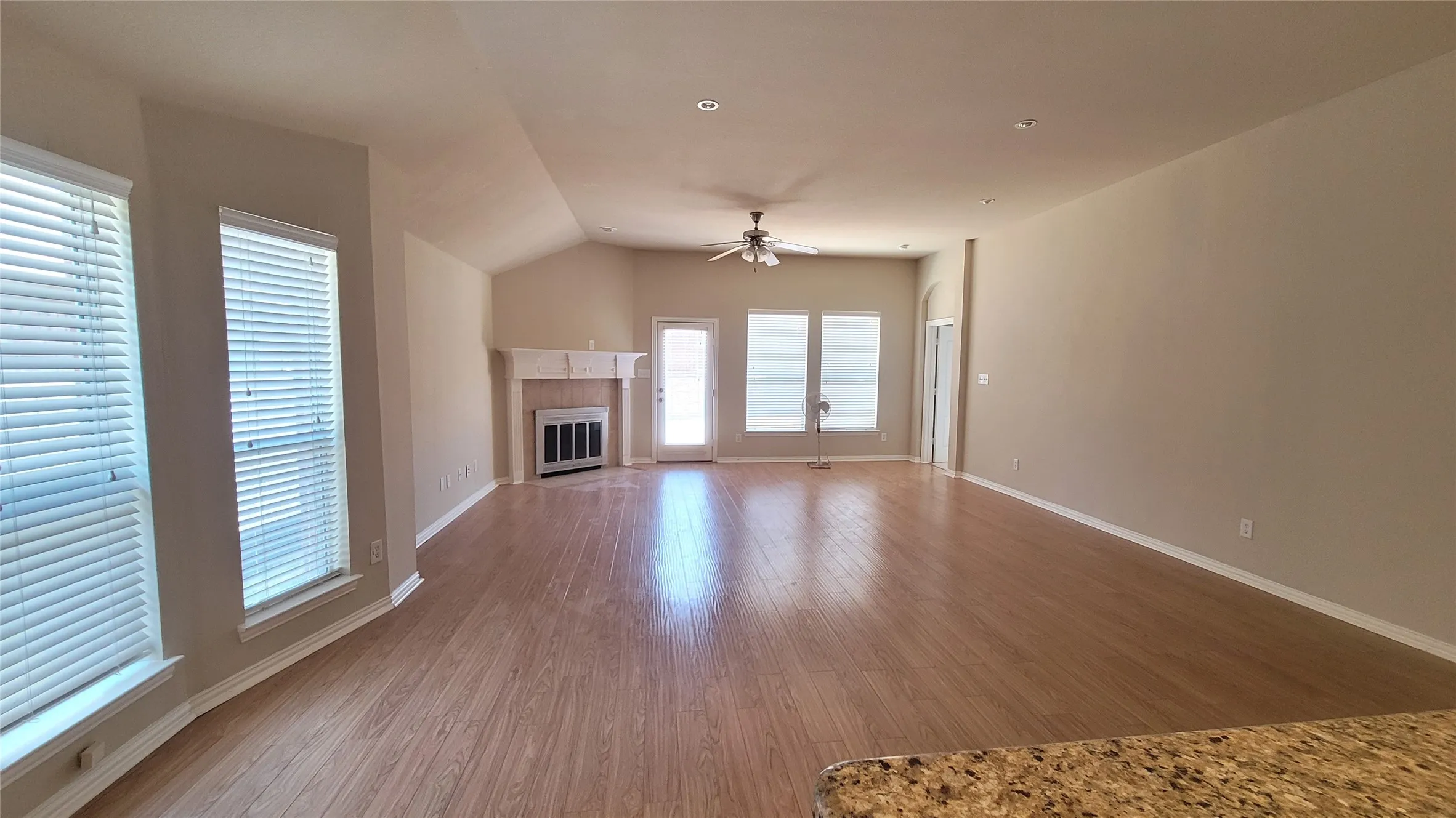 Spacious living area featuring wood-finish flooring, vaulted ceiling, and a fireplace with a mantel