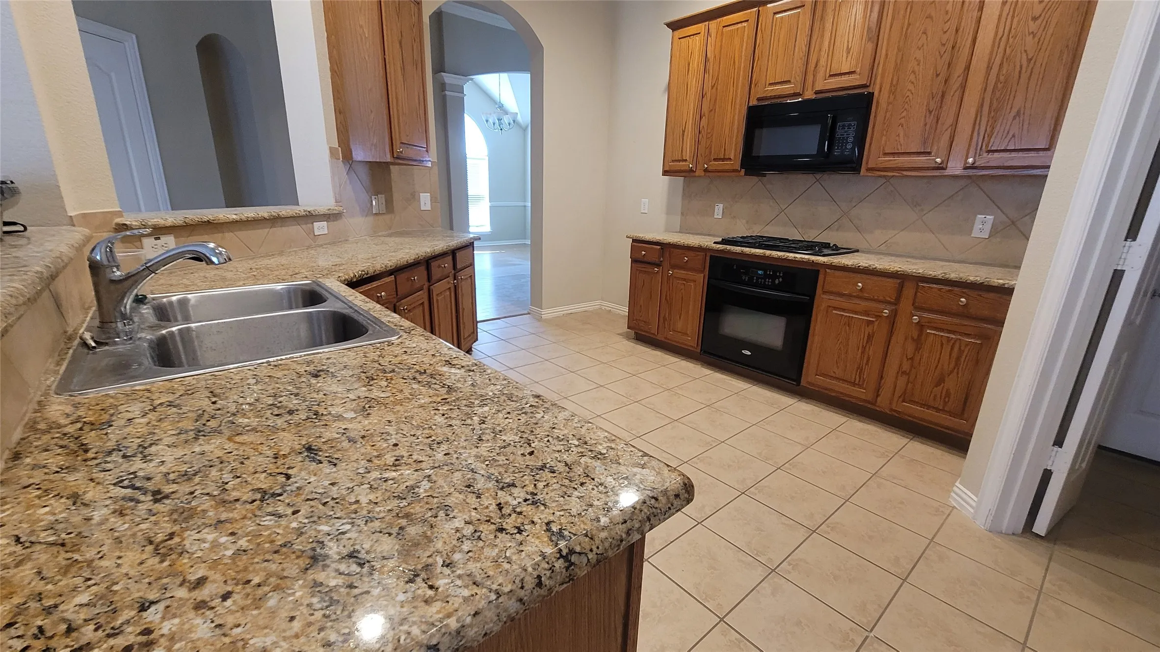 Kitchen featuring granite countertops, wood cabinetry, tile flooring, a double basin sink, and integrated black appliances