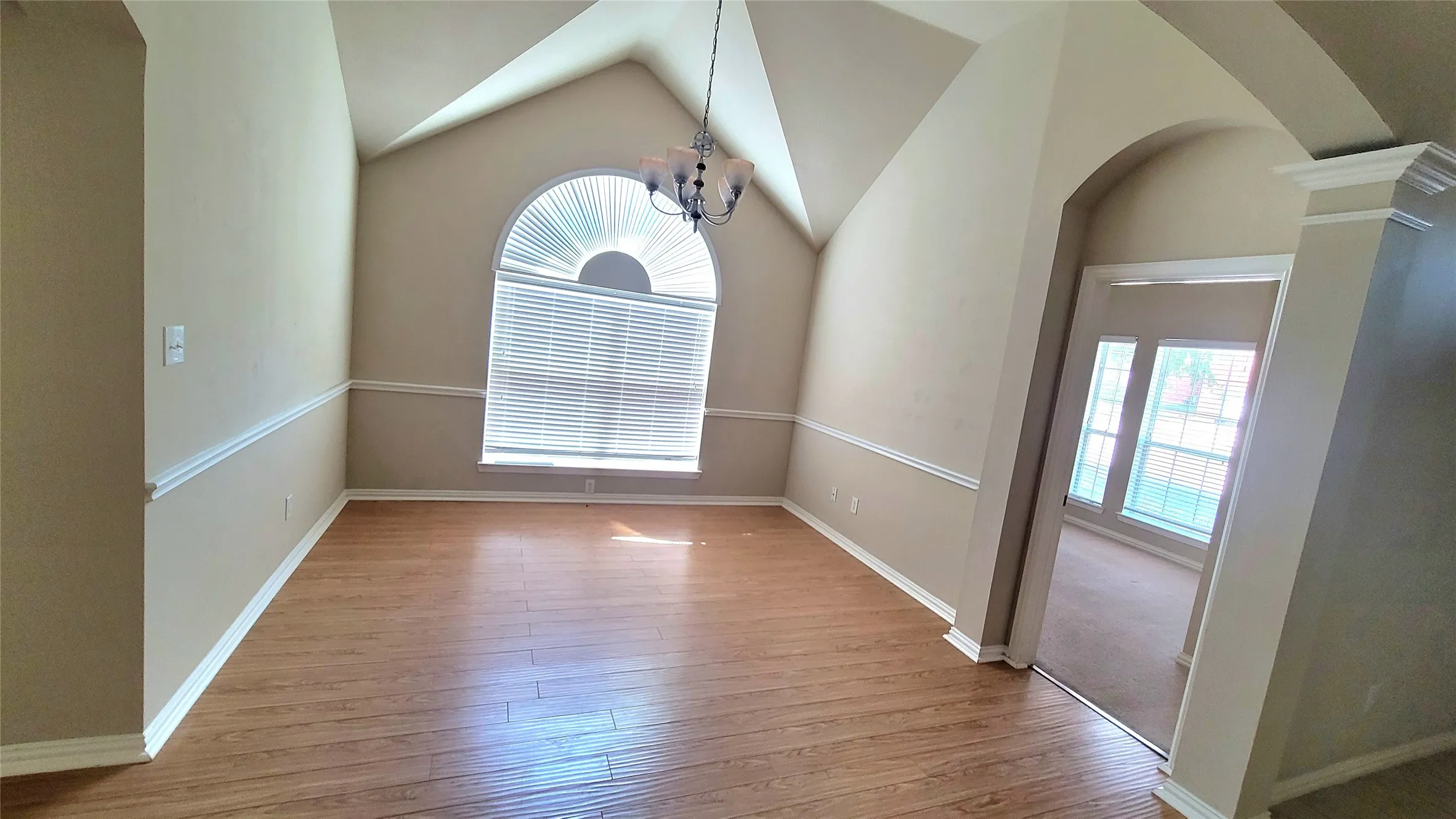 Vaulted ceiling, wood-finish flooring, half-round arched window with blinds, decorative chair rail molding, and an arched entry