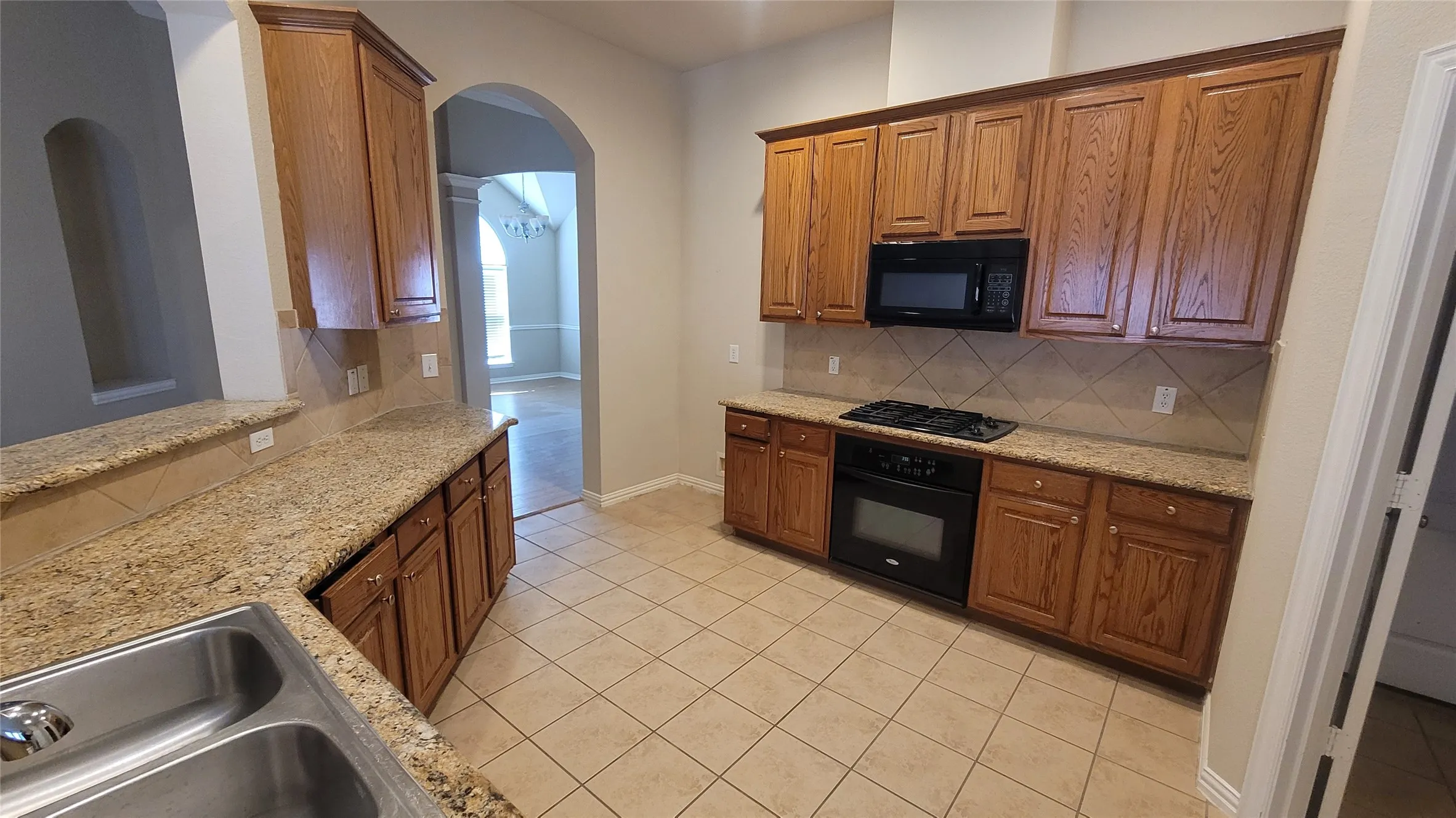 Kitchen featuring abundant wood cabinetry, granite countertops, stainless steel double-basin sink, black built-in oven, and a black microwave