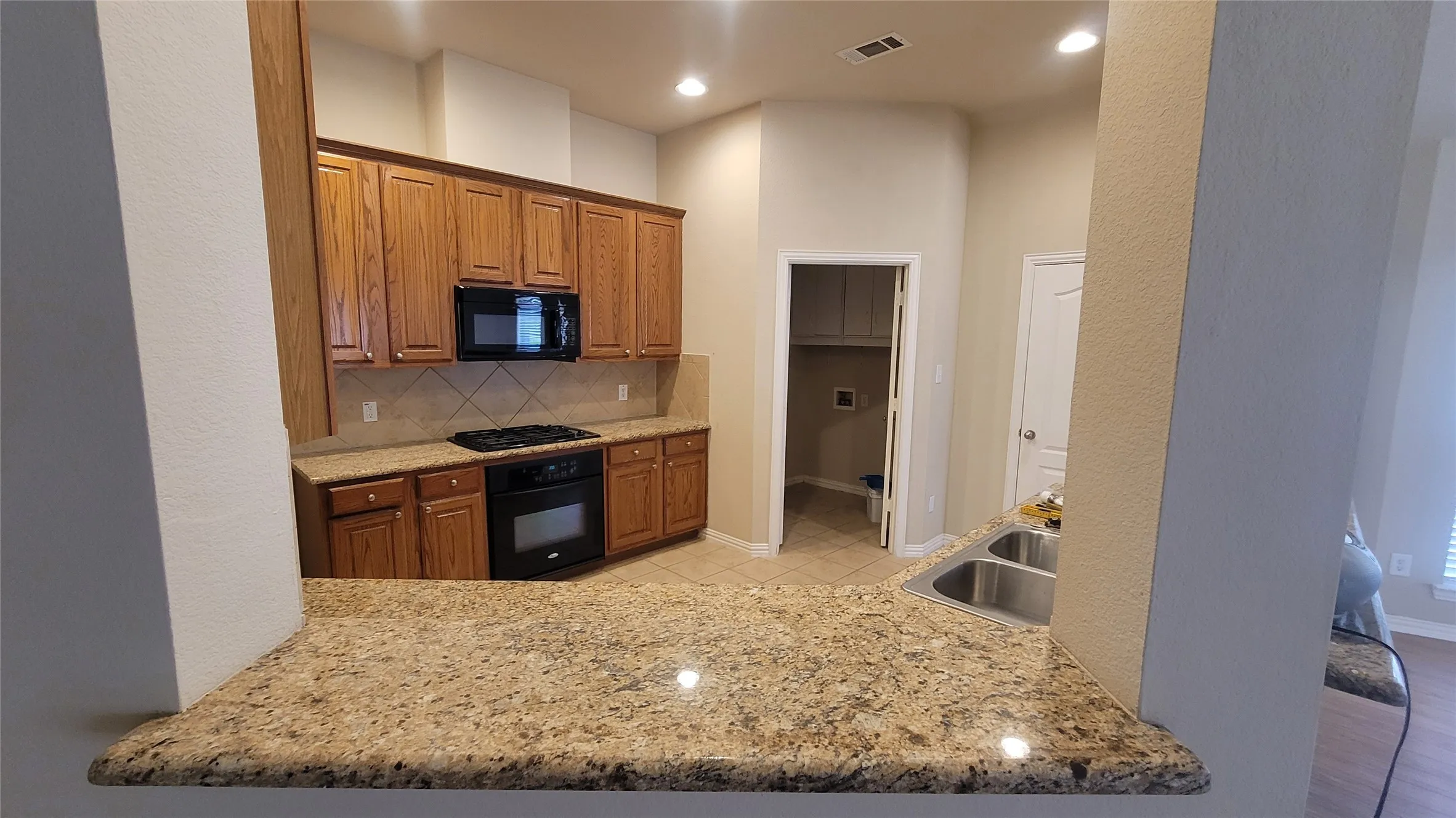 Kitchen featuring wood cabinetry, granite countertops, a built-in microwave, a gas range, and a dual-basin sink