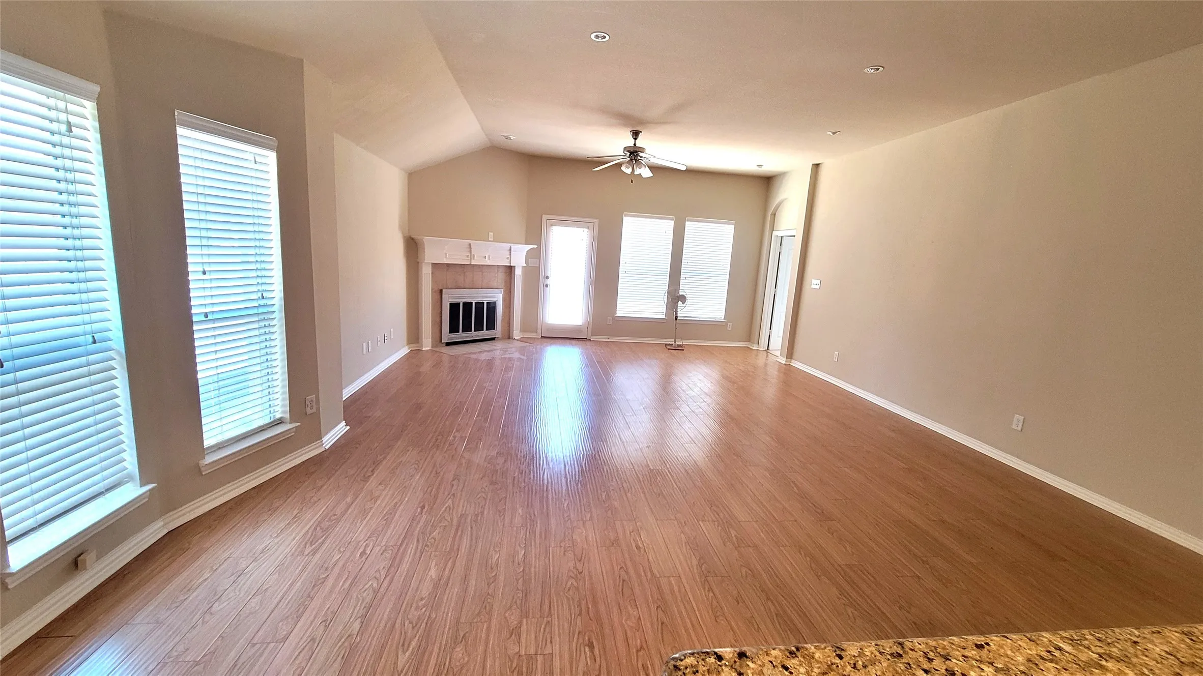 Wood-finish flooring, vaulted ceiling, central ceiling fan, fireplace with a mantle, and multiple windows