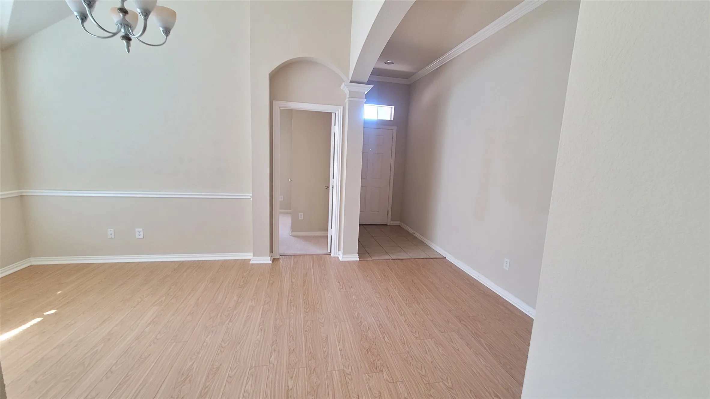 Wood-finish flooring, arched entryway, crown molding, chair rail, and a semi-flush mount chandelier