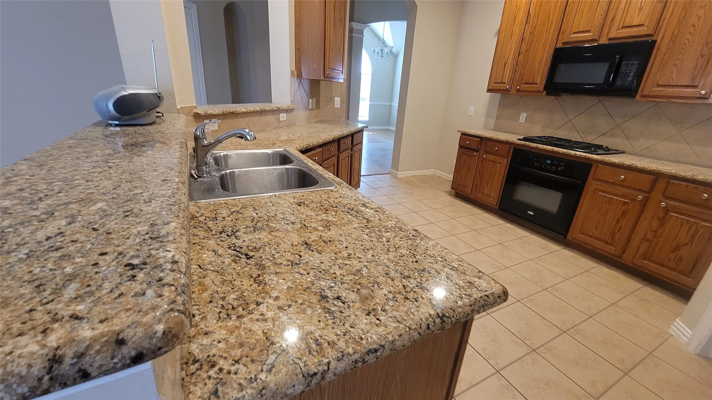 Granite countertops, double basin stainless steel sink, tile flooring, wood cabinetry, and built-in black appliances
