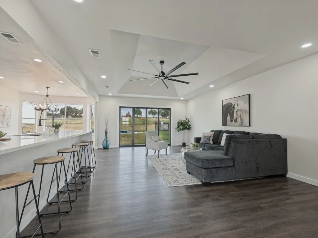 Expansive living area with wood-finish flooring, recessed lighting, and a tray ceiling with a contemporary fan