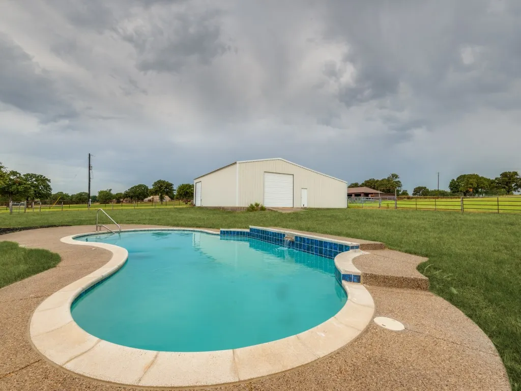 Freeform swimming pool with a stone coping and a waterfall feature, surrounded by an exposed aggregate deck and a manicured lawn