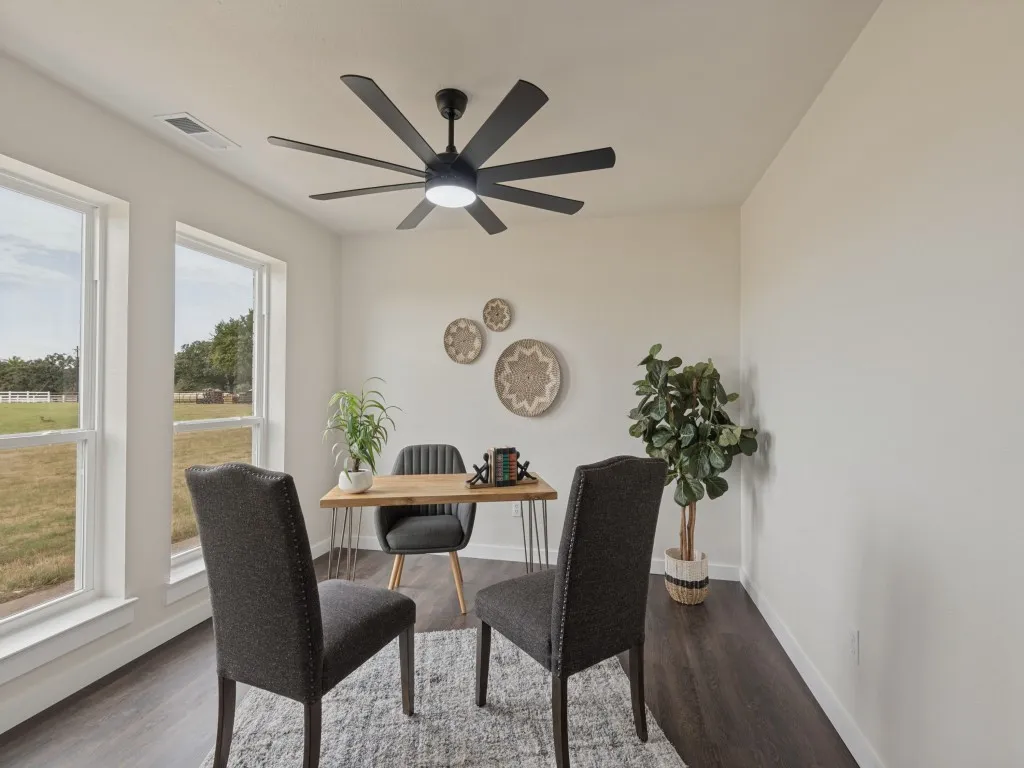 Bright interior space featuring multiple windows, dark wood-finish flooring, a modern black ceiling fan with integrated lighting, and light-toned walls