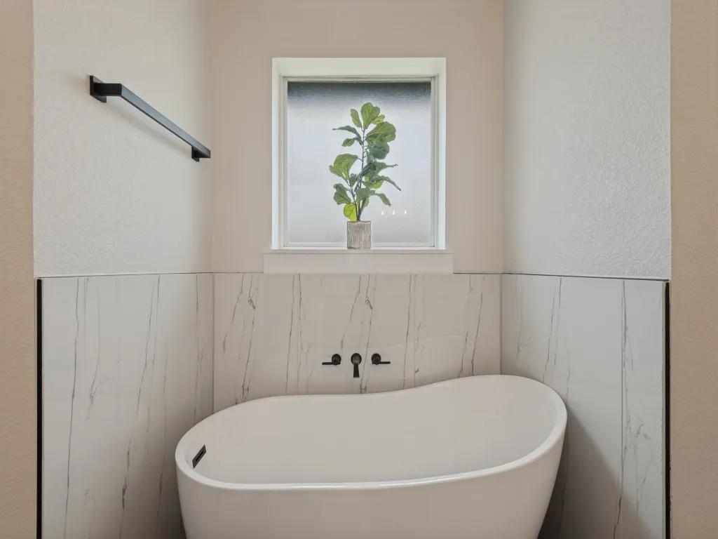 Freestanding soaking tub with matte black fixtures, floor-to-ceiling tile surround, and a frosted window