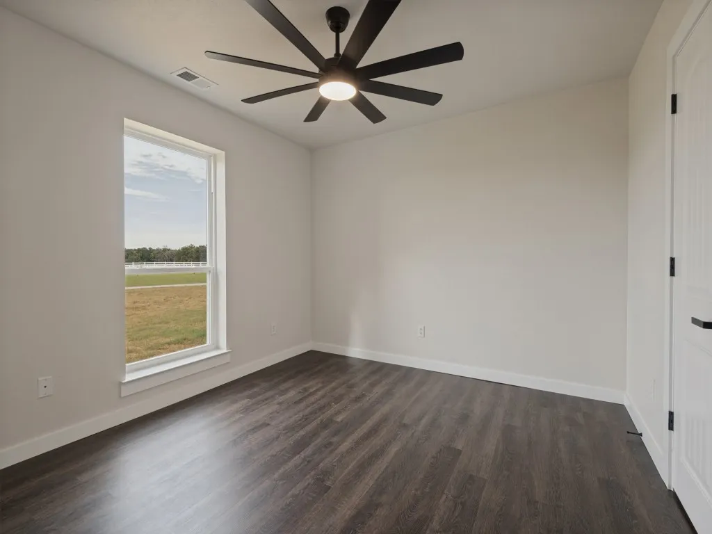 Spacious room featuring wood-finish flooring, a large window, a modern ceiling fan with integrated lighting, and a paneled interior door with matte black hardware