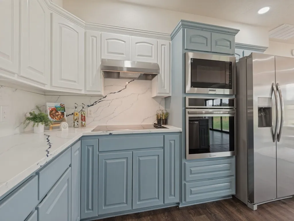 Two-tone cabinetry with white upper and blue lower cabinets, stainless steel appliances, white countertops with black veining, and wood-finish flooring