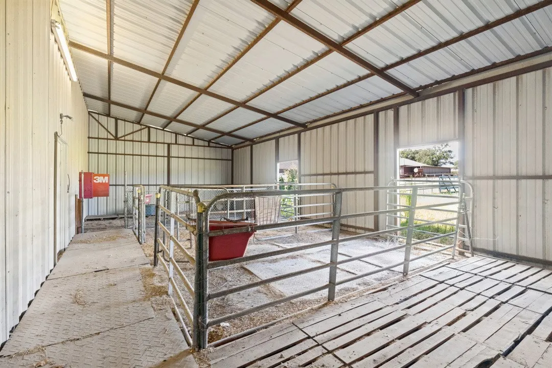 Metal-sided outbuilding featuring a sloped metal roof, exposed structural beams, and integrated animal pens