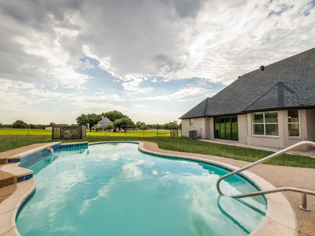 Curved swimming pool with tiled steps, a water feature, and integrated handrails