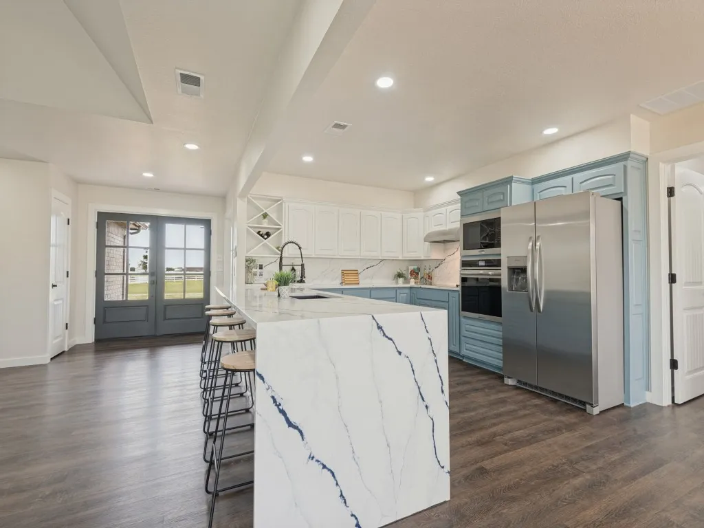 Kitchen featuring a substantial island with stone countertop, stainless steel appliances, two-tone cabinetry, and wood-finish flooring