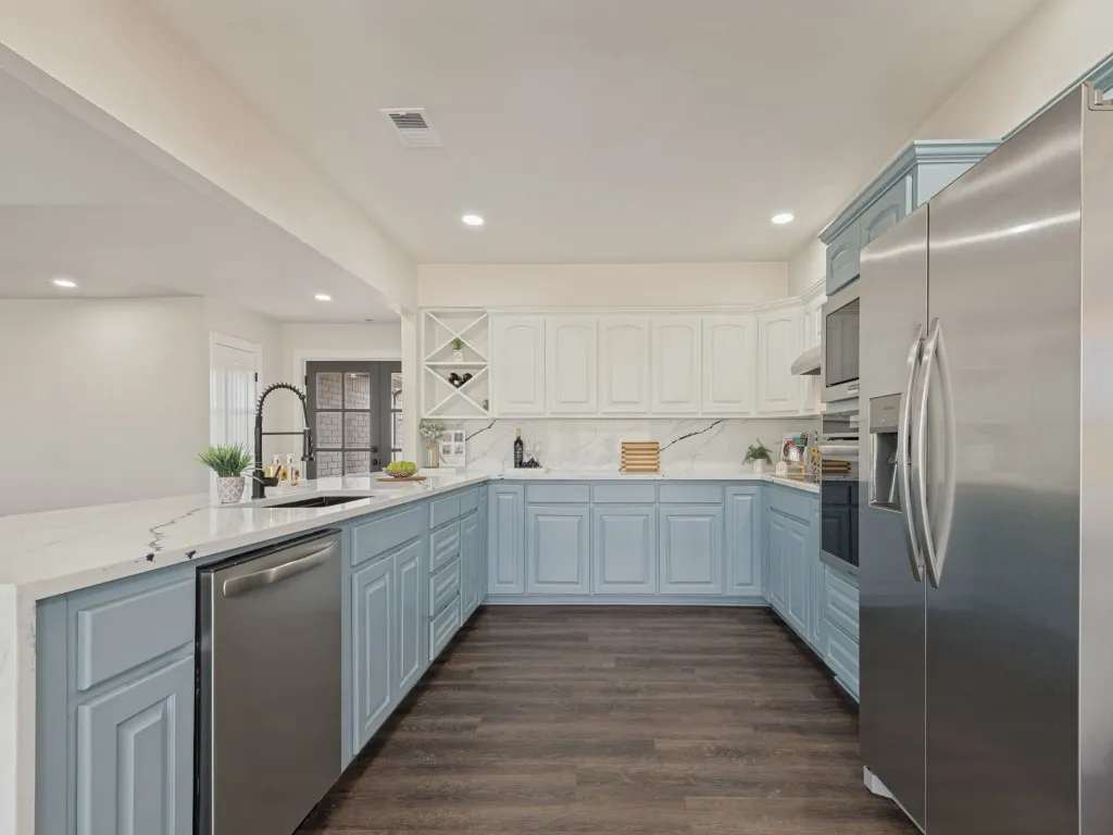 U-shaped kitchen with white and blue cabinetry, white countertops, stainless steel appliances, and dark wood-finish flooring