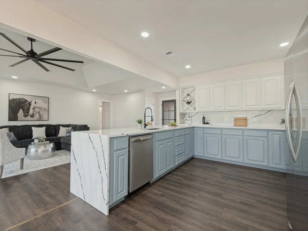 Kitchen featuring a waterfall island, stainless steel dishwasher, full-height backsplash, white upper cabinetry, and contrasting lower cabinetry