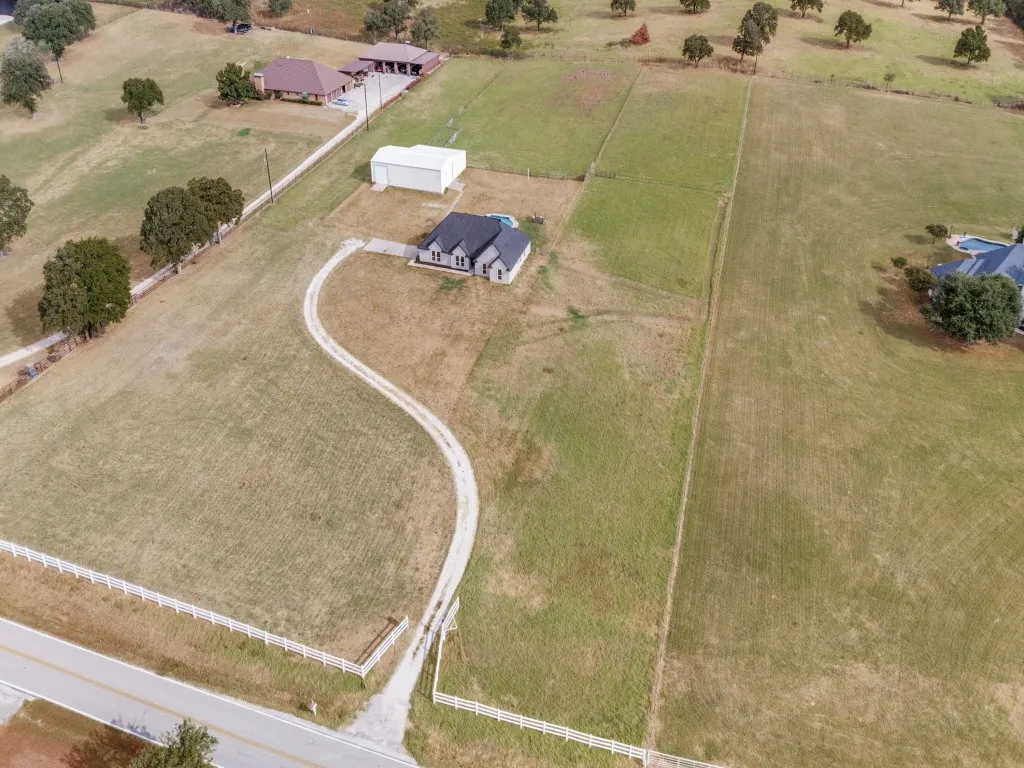 Expansive grass lot featuring a winding driveway, white fencing, and an outbuilding