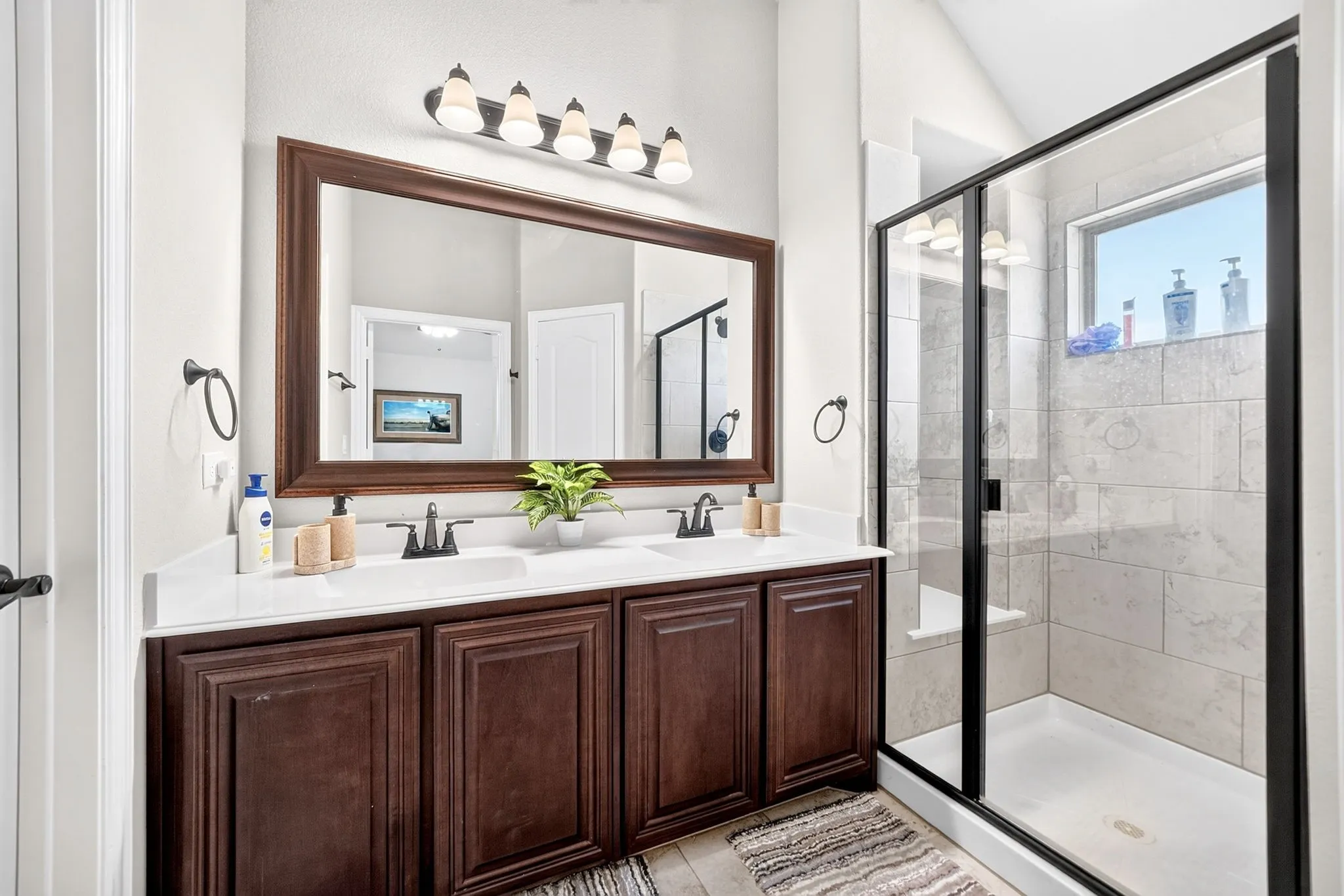 Dual vanity with integrated sinks, framed mirror, dark wood-finish cabinetry, and a frameless glass shower enclosure with a built-in bench