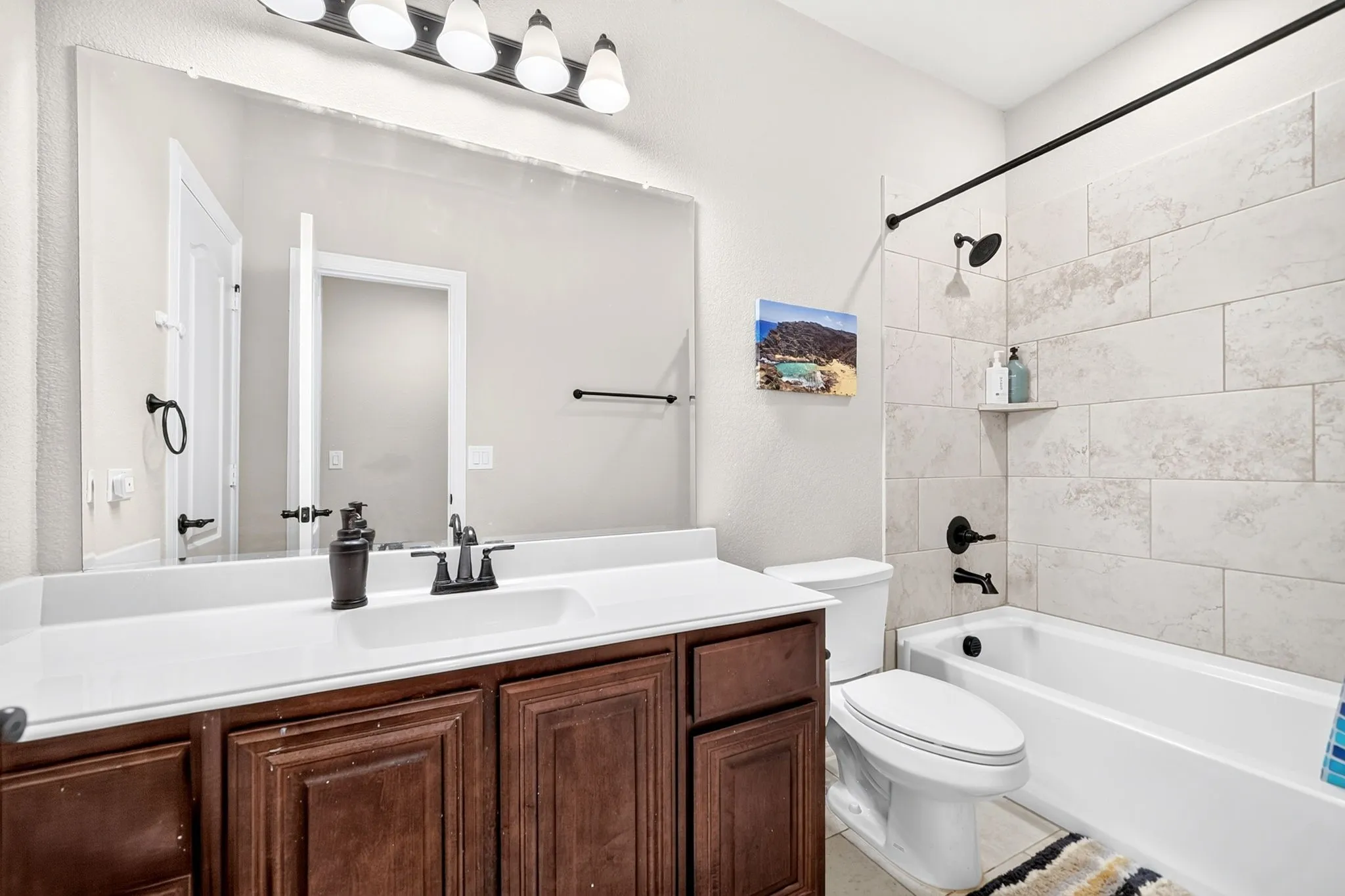 Bathroom featuring a spacious vanity with wood-finish cabinetry, a large mirror, and a full bathtub with a tiled surround