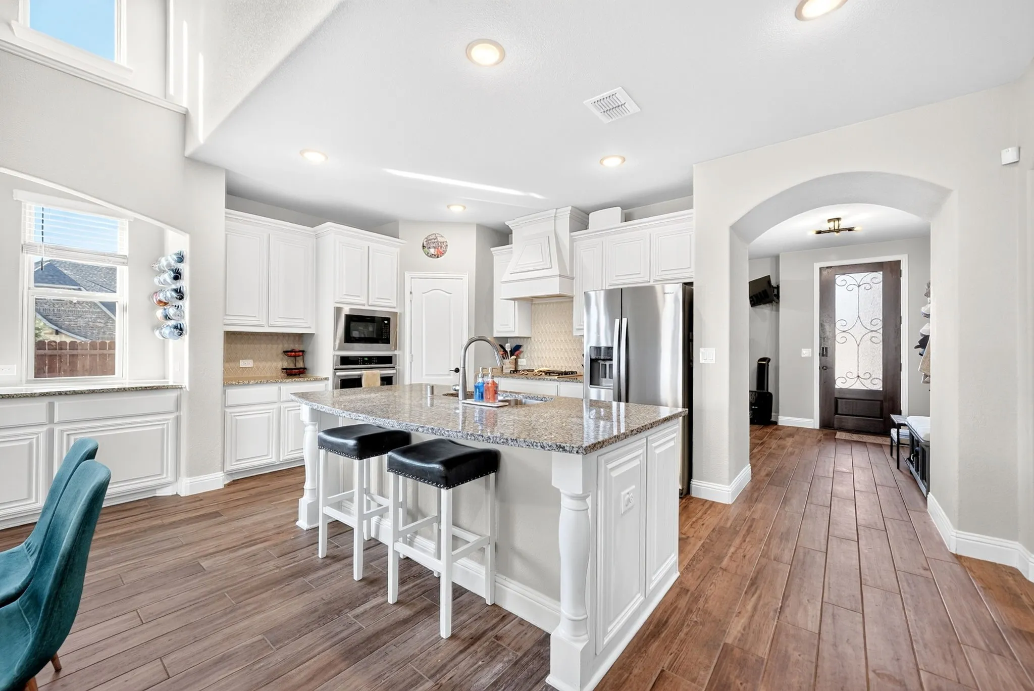 Kitchen with wood-finish flooring, white cabinetry, stainless steel appliances, a center island with bar seating, and a built-in buffet with a window
