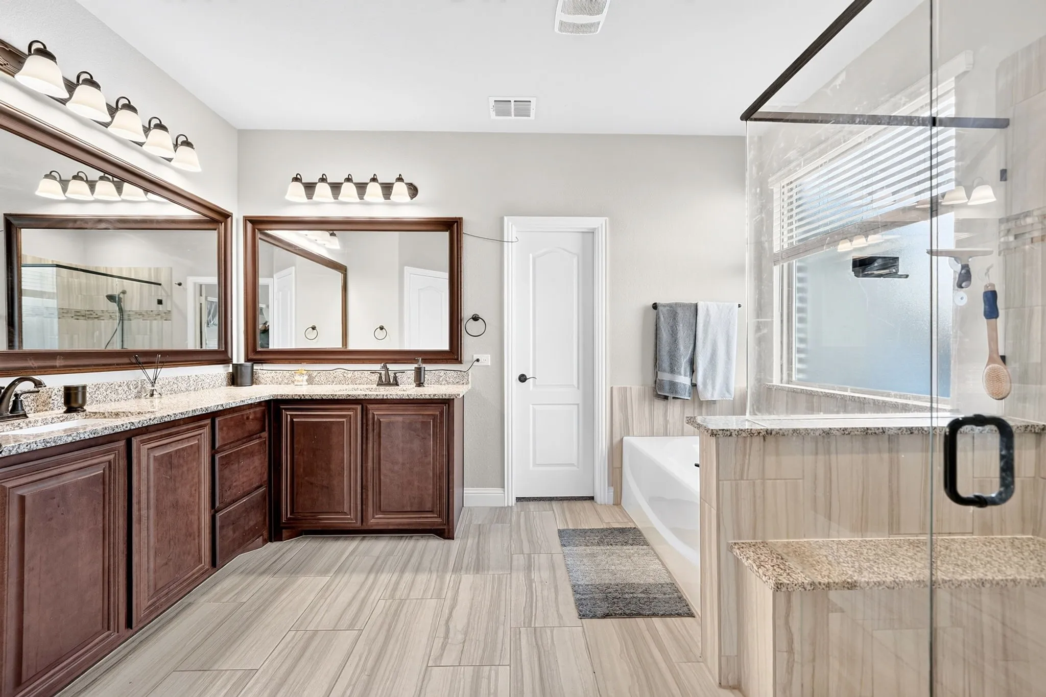 Dual vanity with dark wood-finish cabinetry, light-toned countertop, and framed mirrors