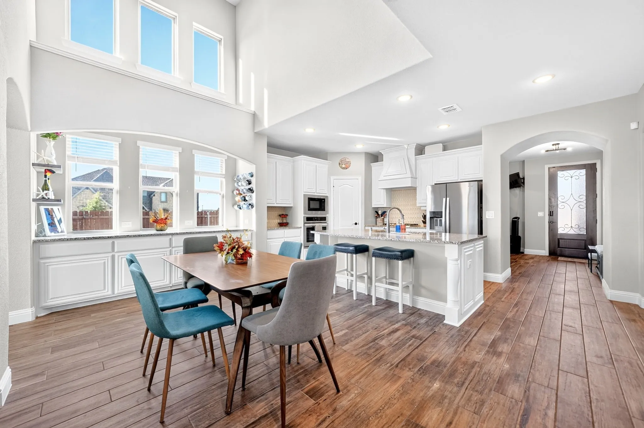 Expansive open-concept living area featuring high ceilings, wood-finish flooring, a kitchen island with seating, a built-in buffet, and abundant natural light from multiple windows