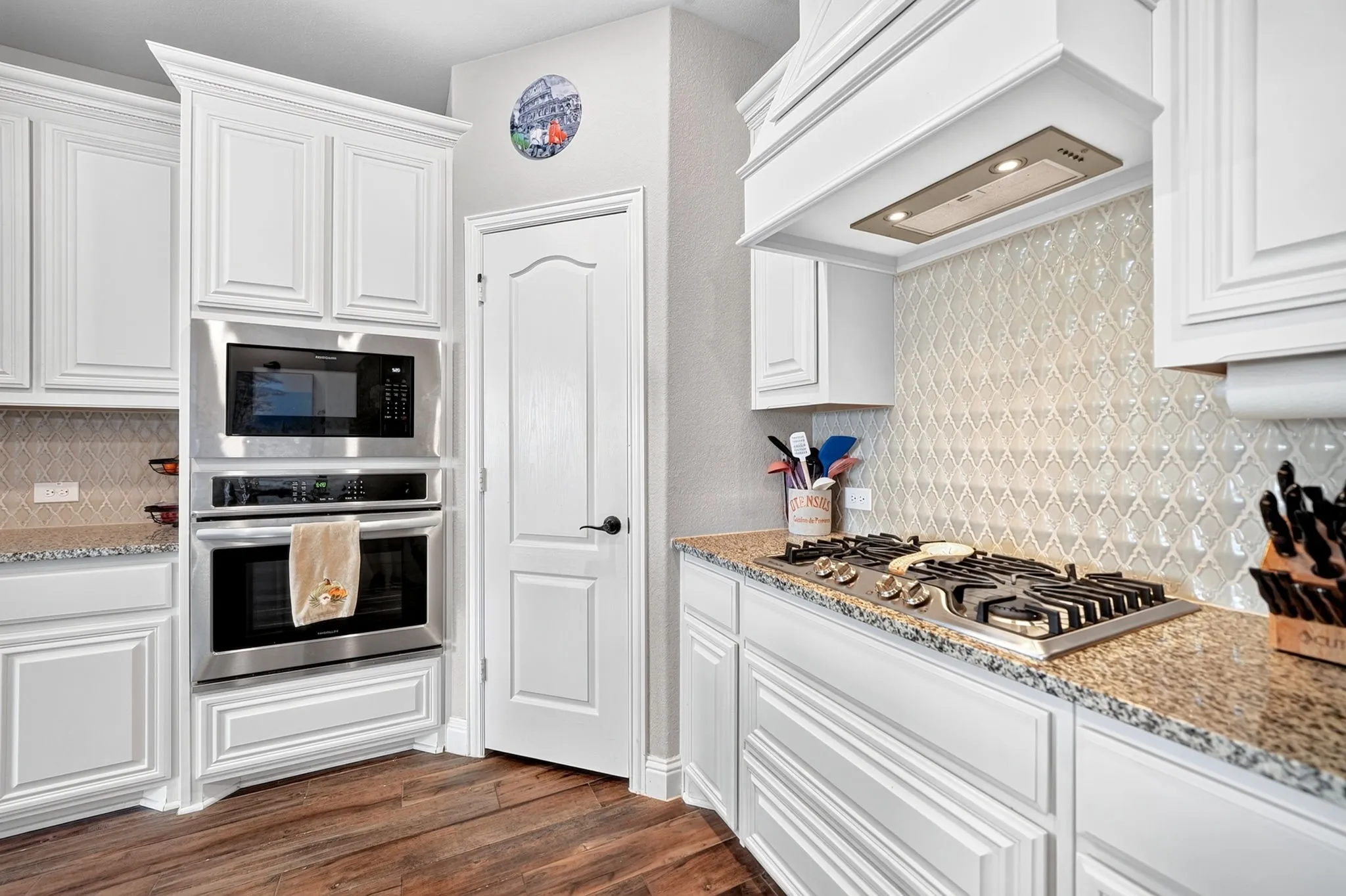White cabinetry with recessed panel doors, built-in stainless steel appliances, granite countertops, and a decorative tile backsplash