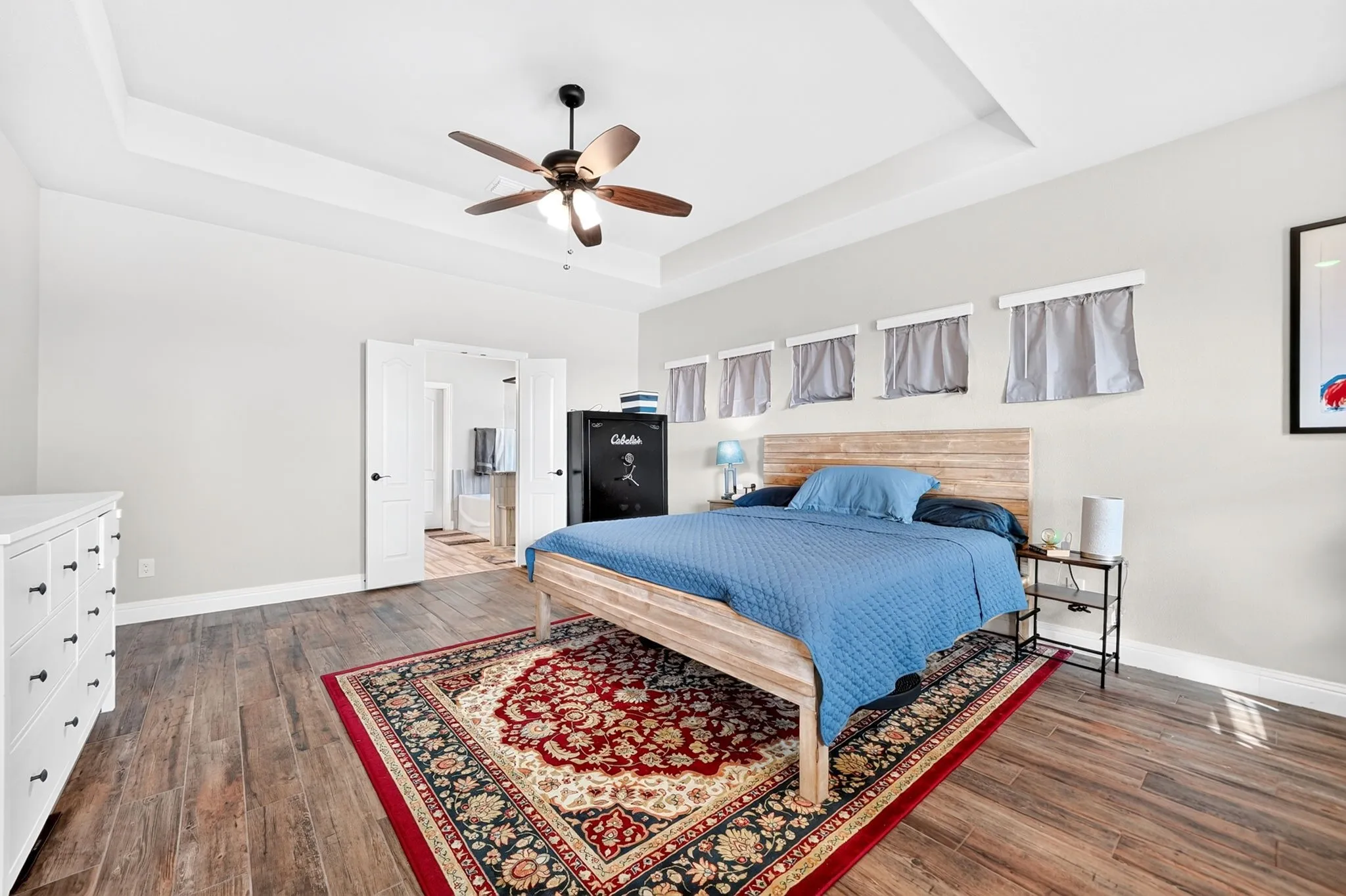Tray ceiling, ceiling fan with light, wood-finish flooring, white double doors, light-toned walls