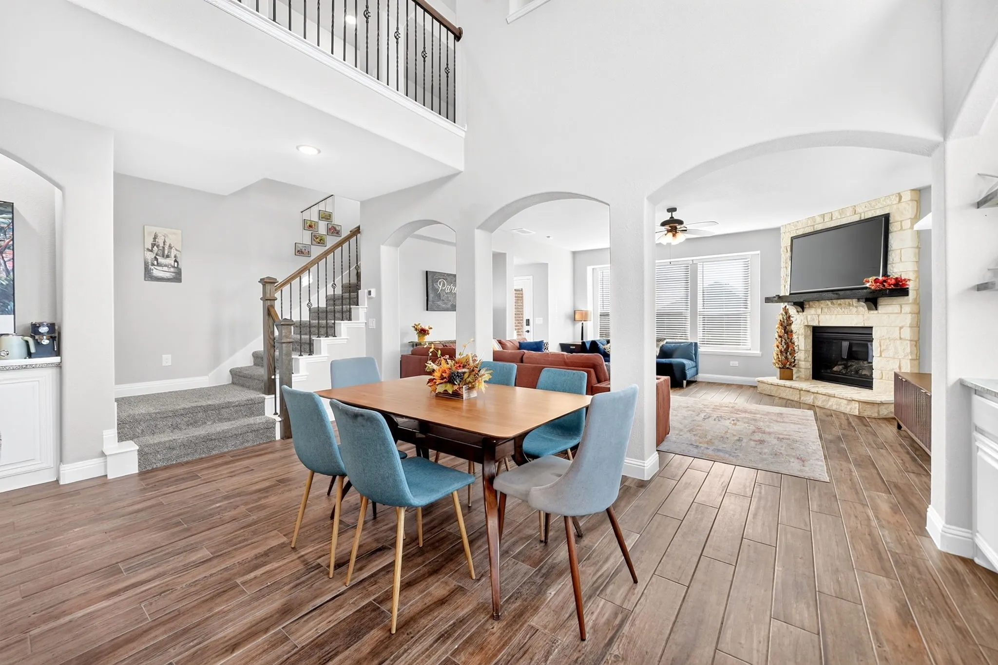 Wood-finish flooring, staircase with wrought iron balusters, stone-clad fireplace with mantel, white cabinetry, and arched doorways