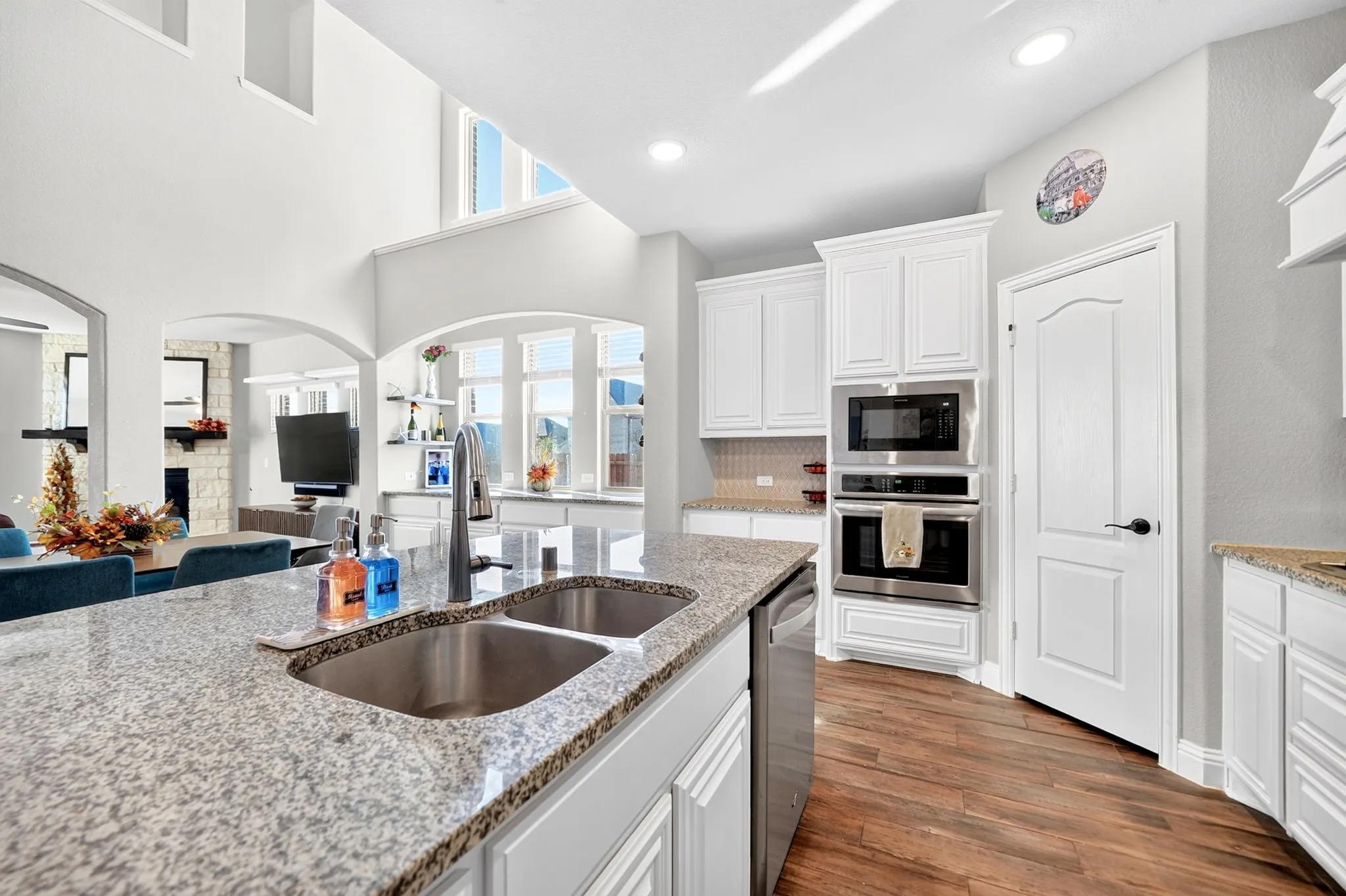 Kitchen featuring wood-finish flooring, white cabinetry, a built-in stainless steel double oven, and a double basin sink with a high-arc faucet
