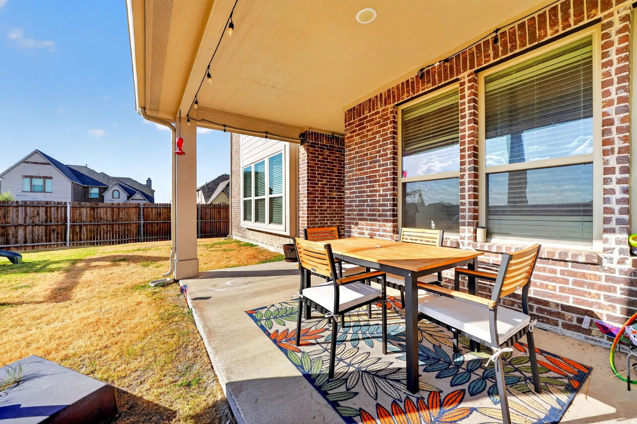 Covered patio featuring string lighting, a concrete slab, and brick exterior walls