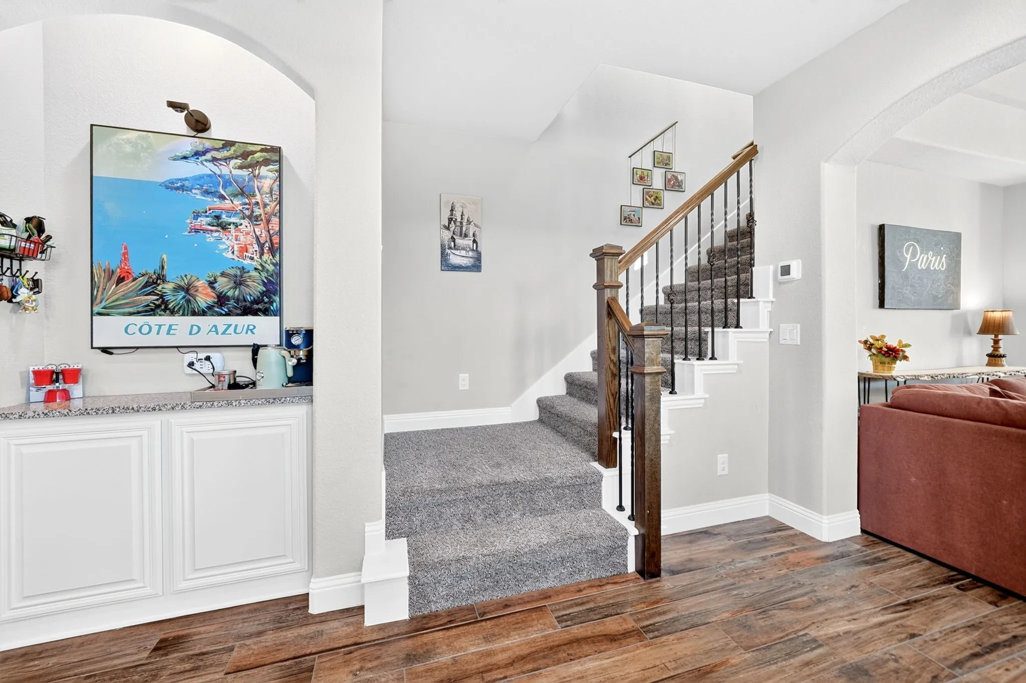 Wood-finish flooring, built-in white cabinetry with a speckled countertop, staircase with wood newel posts and handrail, and carpeted stairs
