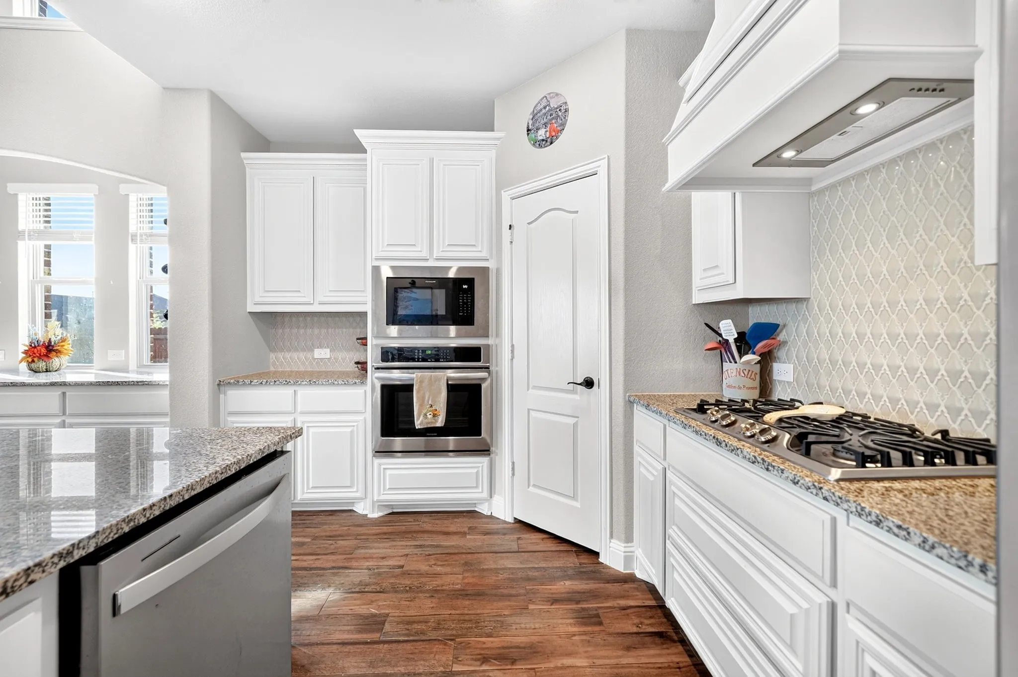Gourmet kitchen featuring white cabinetry, granite countertops, stainless steel appliances, wood-finish flooring, and a decorative tile backsplash