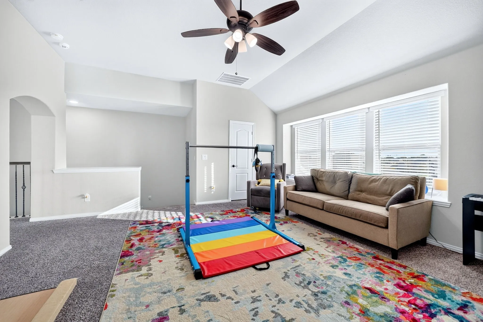Vaulted ceiling, ceiling fan, large windows with blinds, gray carpet, white interior doors