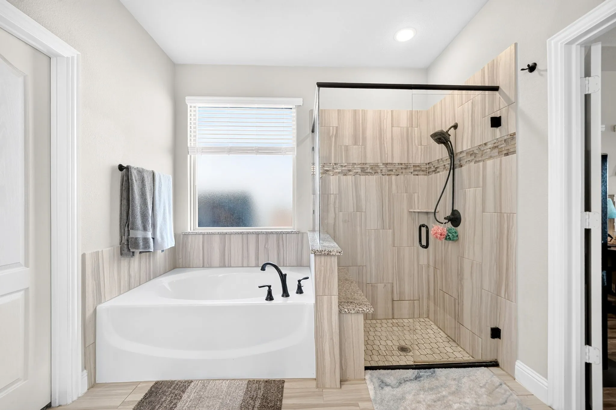 Soaking tub with black fixtures, walk-in shower with tiled walls and built-in bench, glass shower enclosure, and tiled flooring