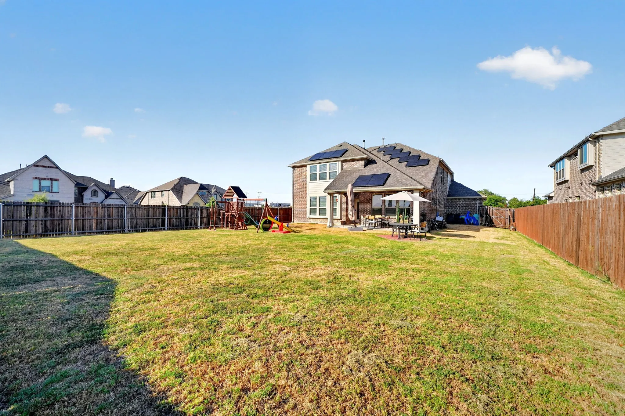 Expansive fenced backyard with a brick and siding exterior and solar panels