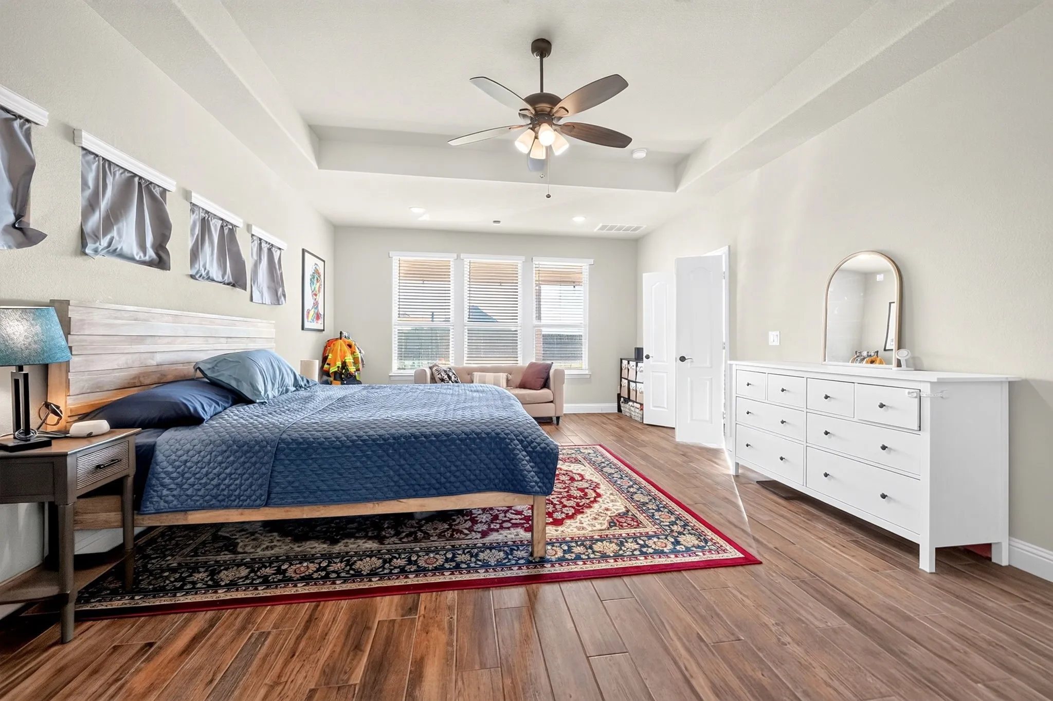 Tray ceiling with a ceiling fan, wood-finish flooring, white paneled doors, and multiple windows
