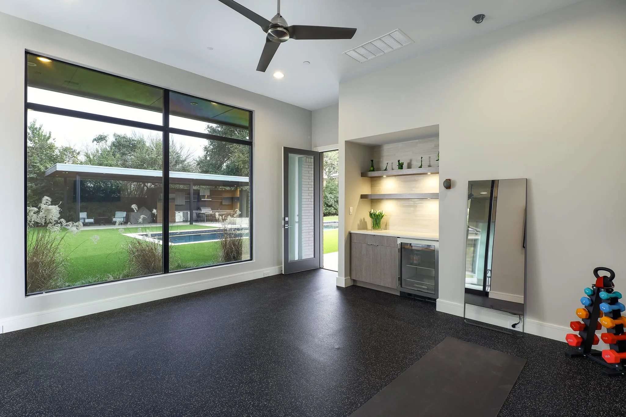 Separate gym with mirrored walls and padded floors overlooking backyard