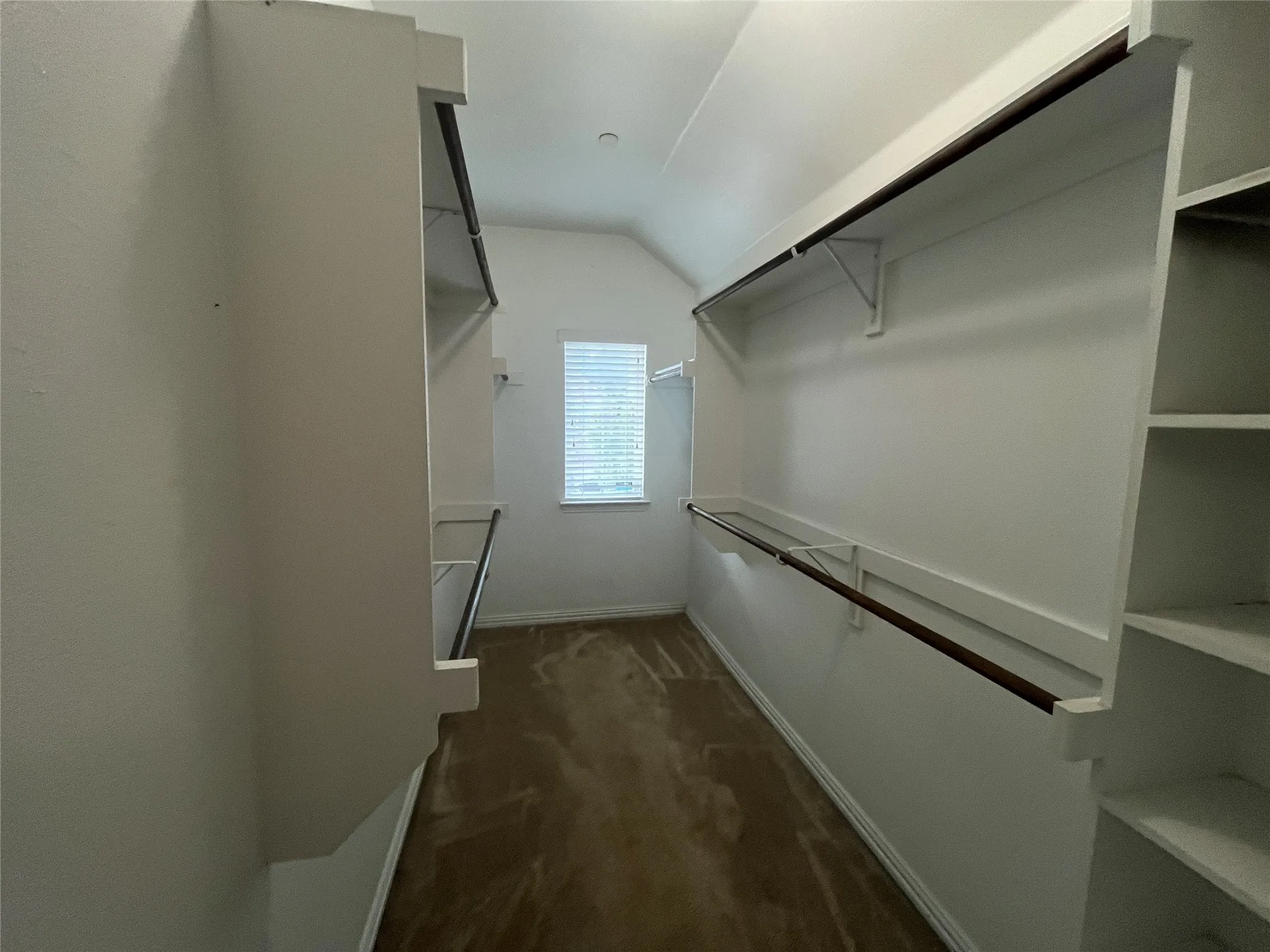 Generous walk-in closet with built-in shelving, multiple hanging rods, and a window with blinds
