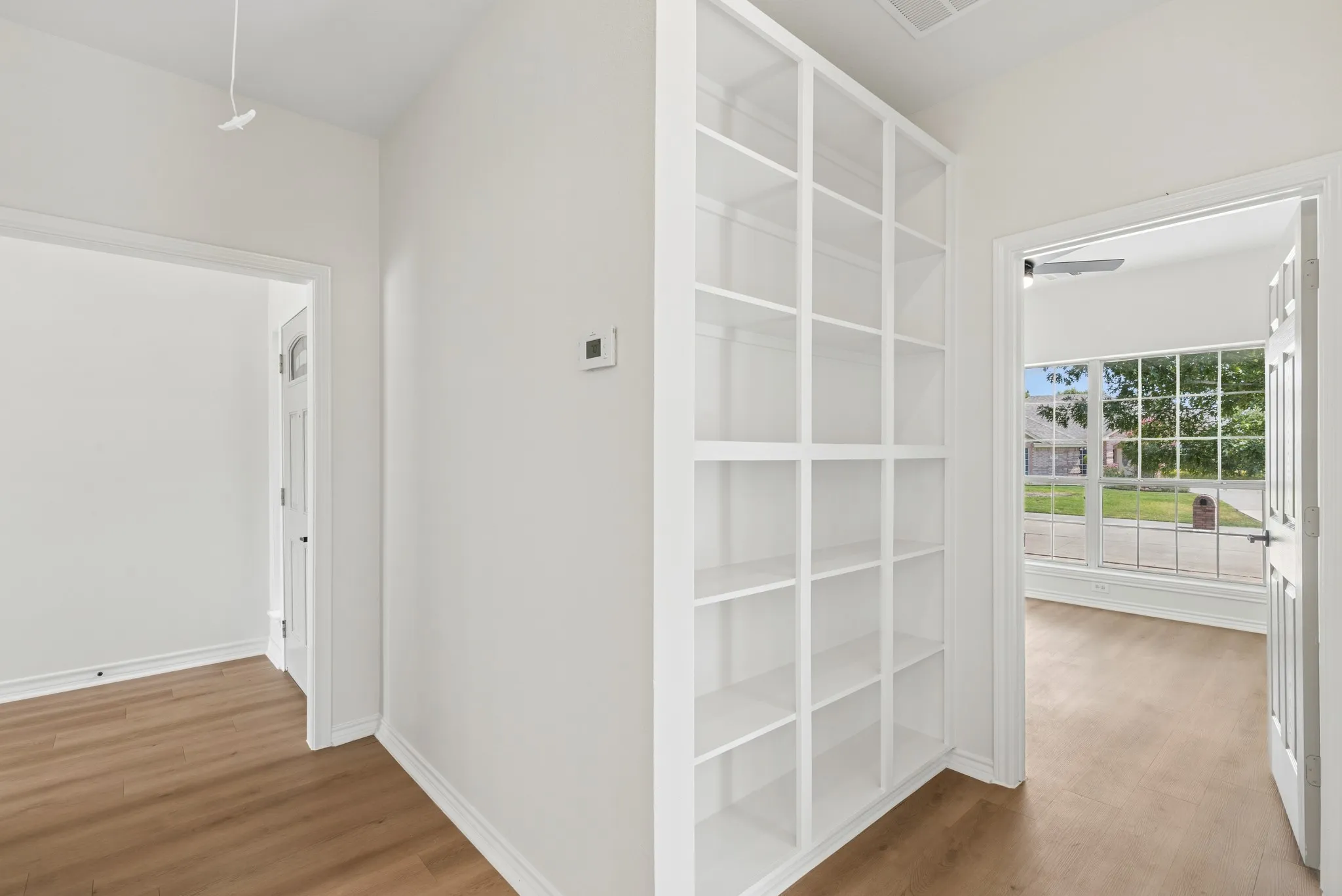 Integrated built-in shelving, wood-finish flooring, white paneled doors, and a large multi-pane window