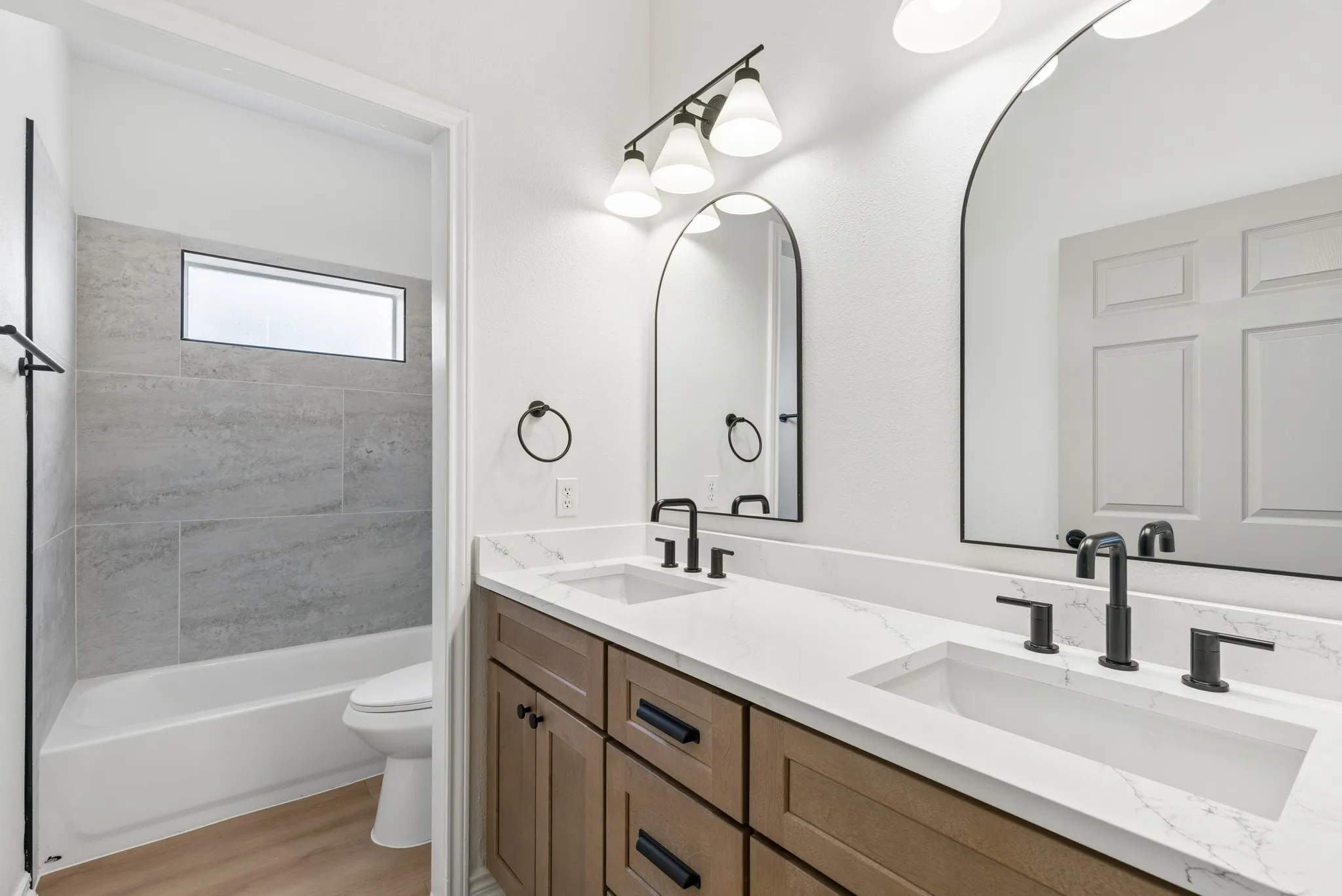 Dual arched mirrors, dual undermount sinks, quartz countertop, wood-finish cabinetry, and matte black fixtures